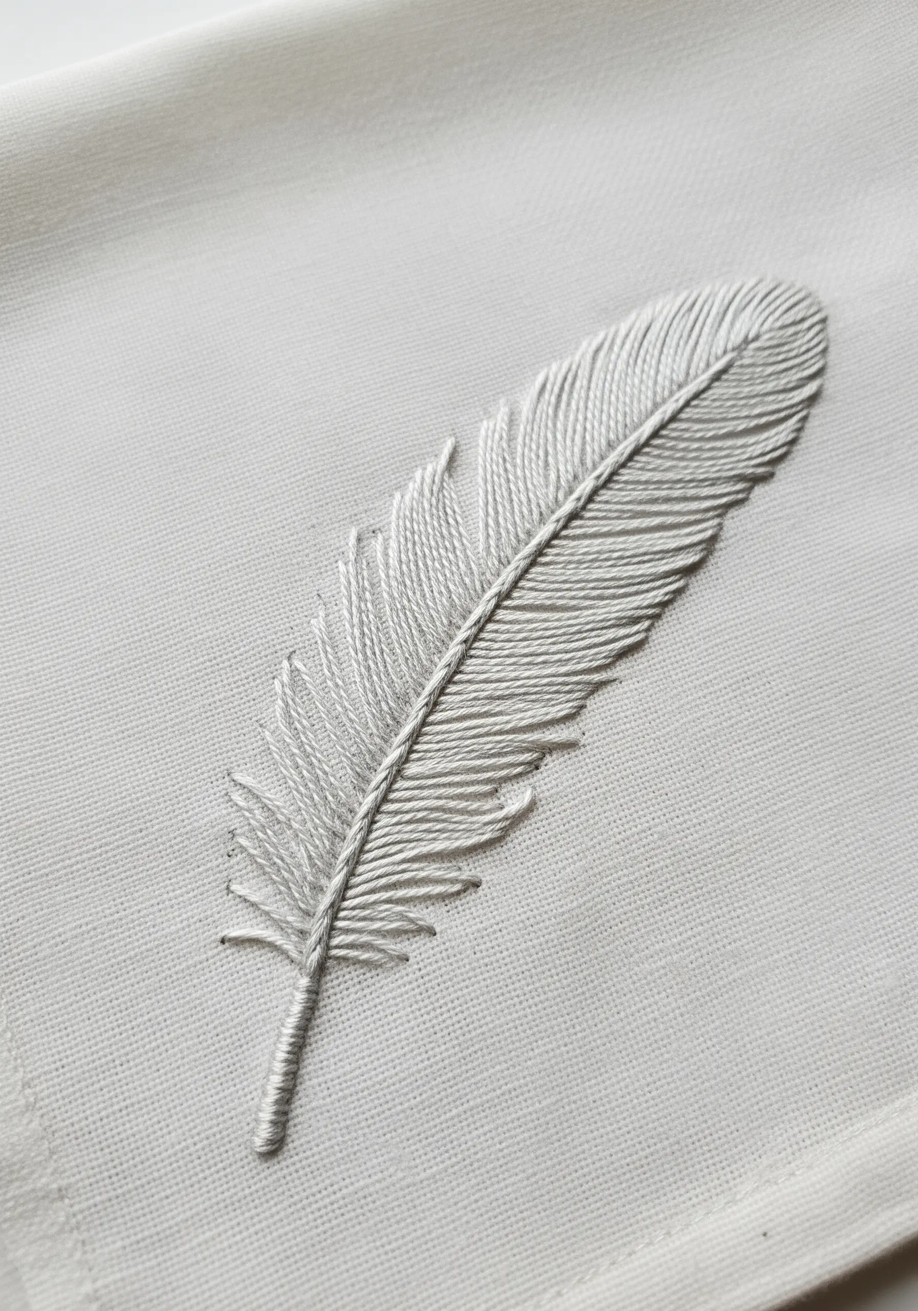 A realistic white feather embroidered in detail using fishbone stitch on a light-colored fabric.