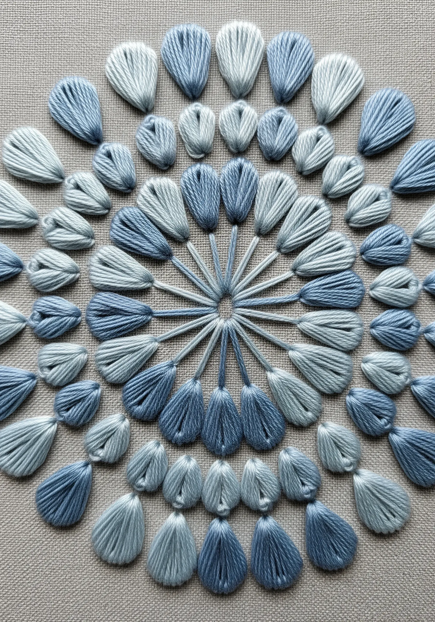 A mandala made of layered teardrop-shaped stitches in shades of blue.