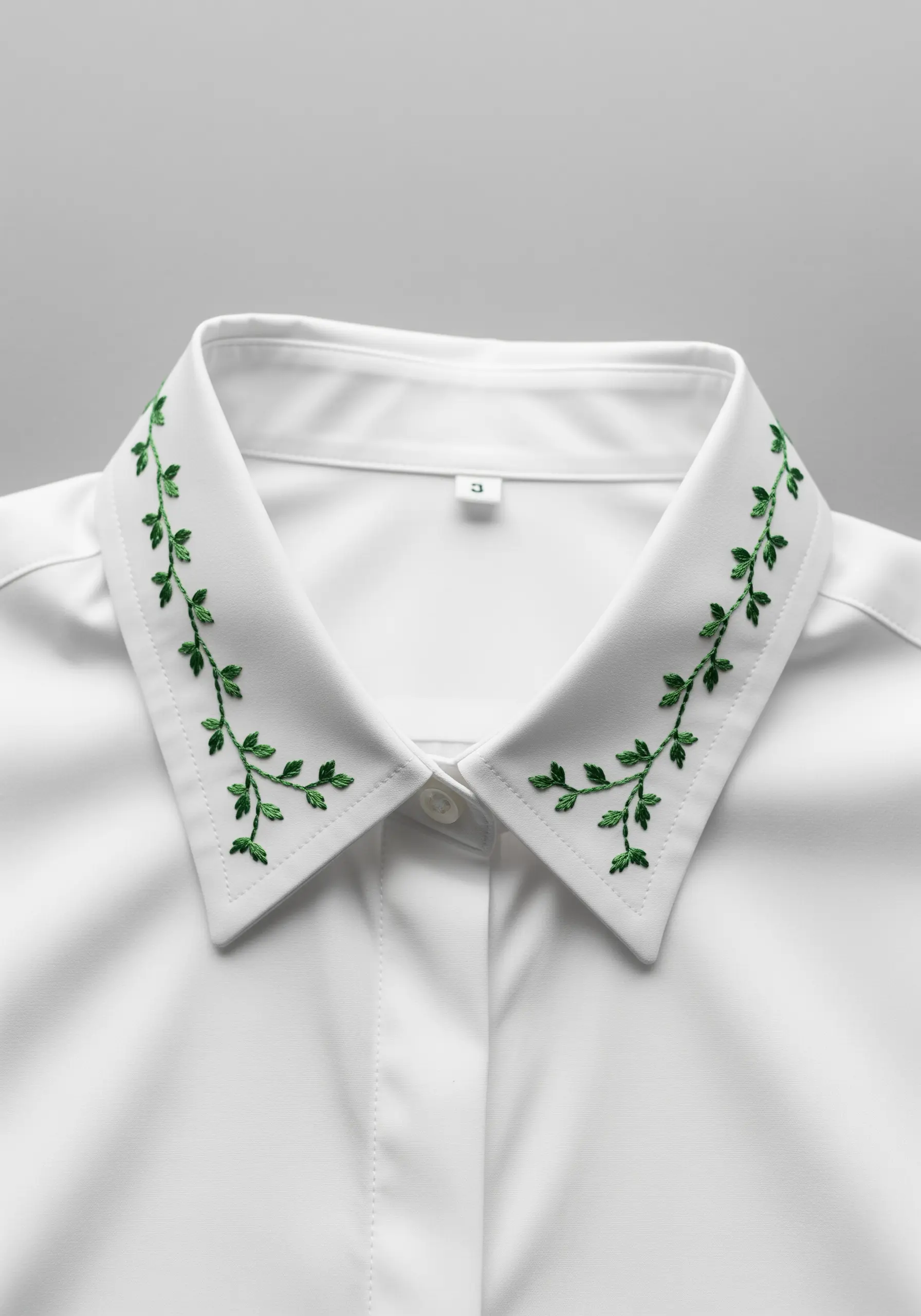 Delicate green vines embroidered along the edges of a crisp white shirt collar.