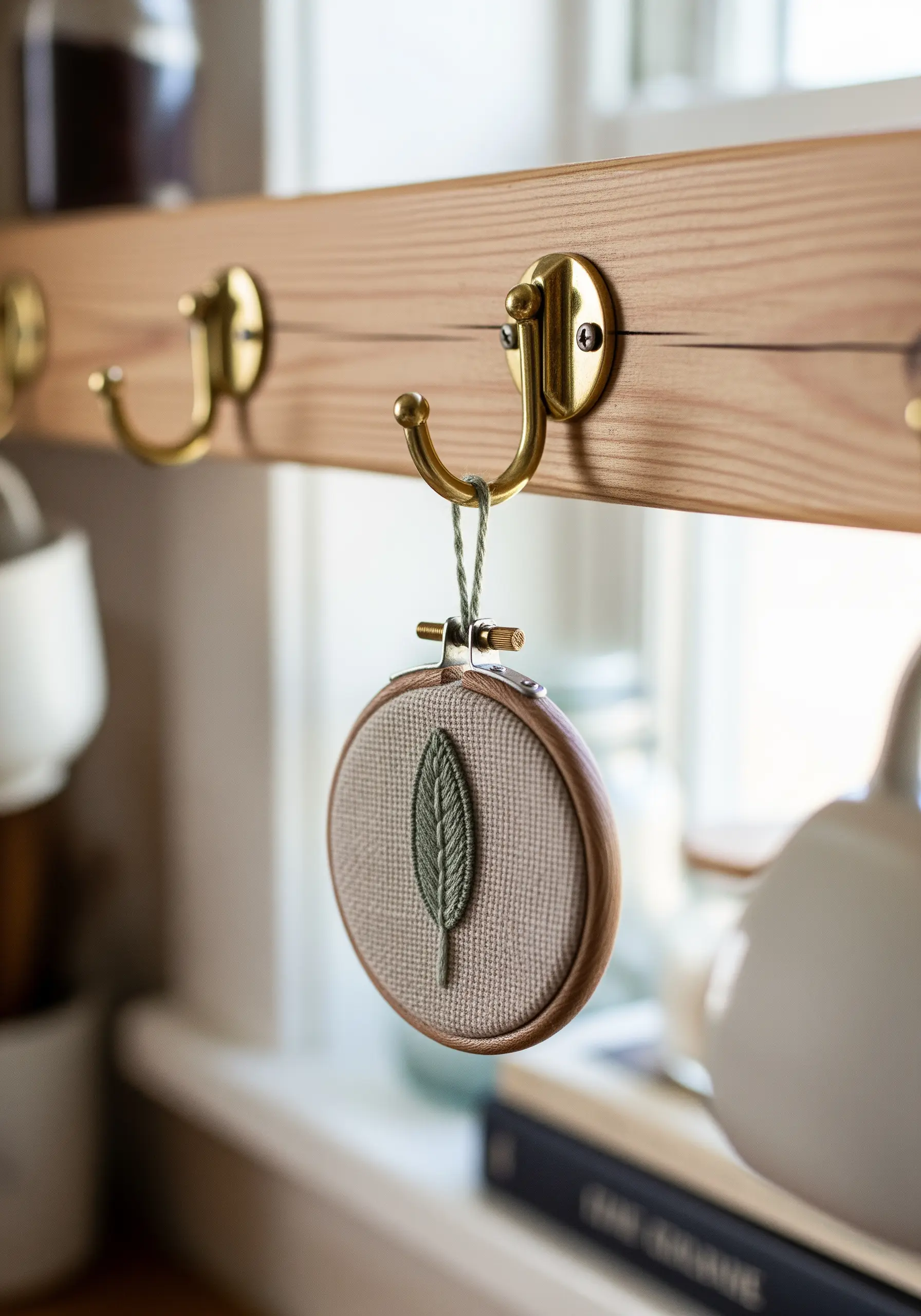 A small embroidery hoop with a single sage leaf, hung from a brass hook in a kitchen.