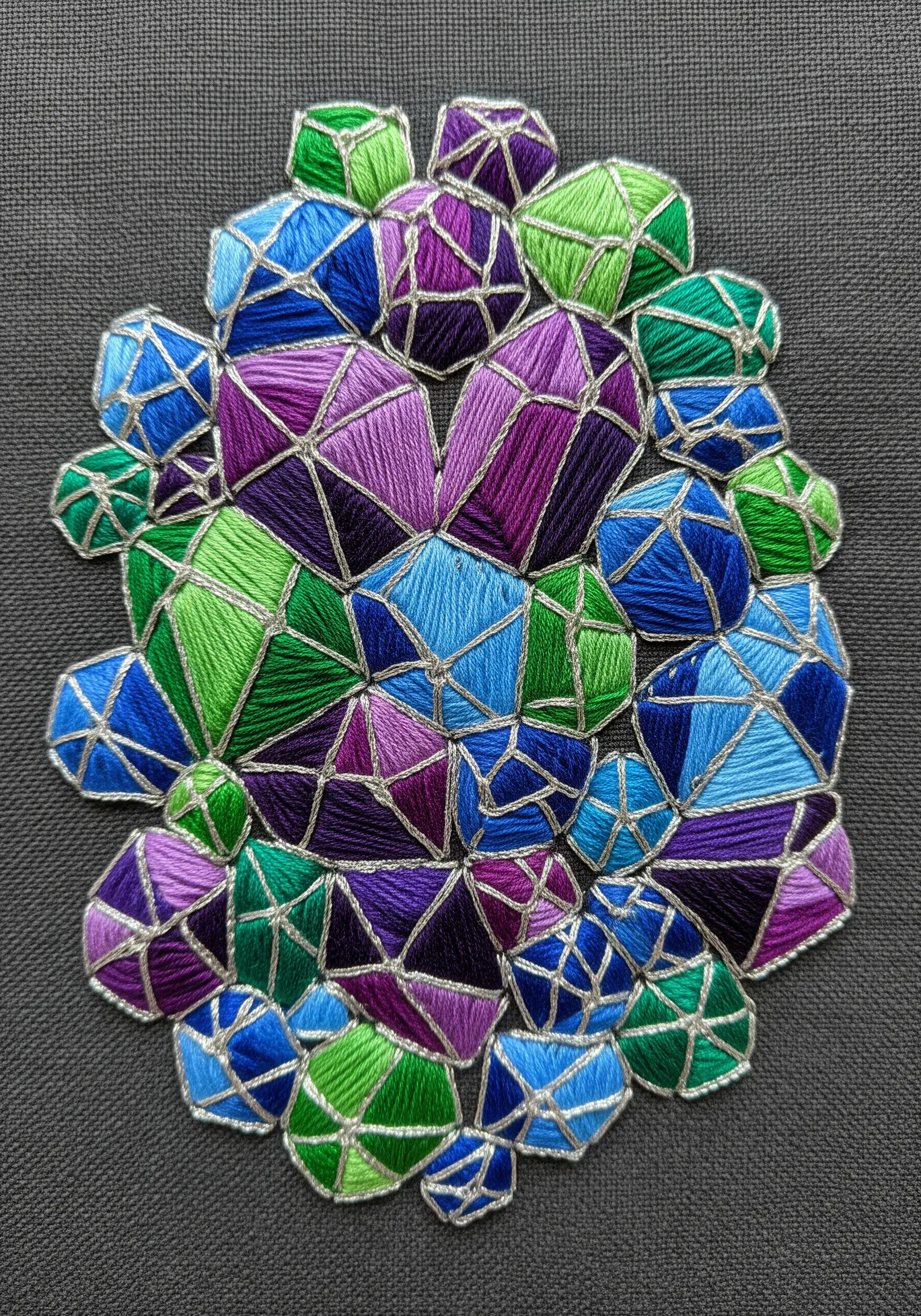 A cluster of geometric shapes filled with satin stitch in blues, greens, and purples, outlined in silver.