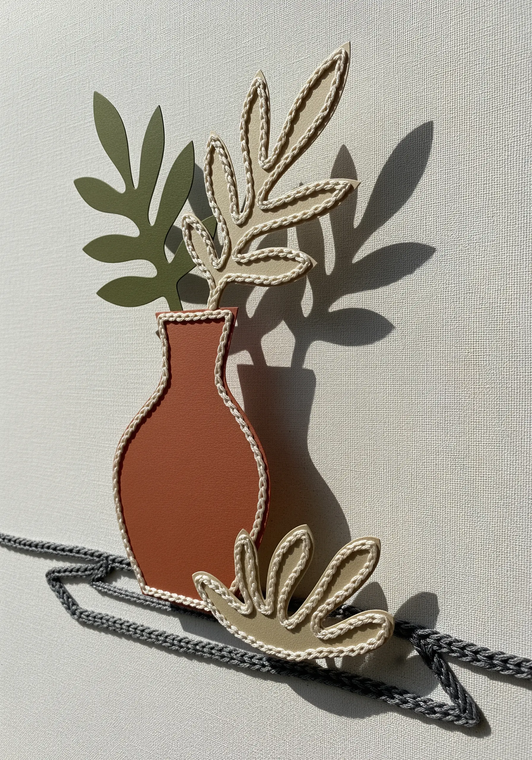 Matisse-style paper cutouts of a vase and leaves, outlined with thick, braided neutral-toned thread.