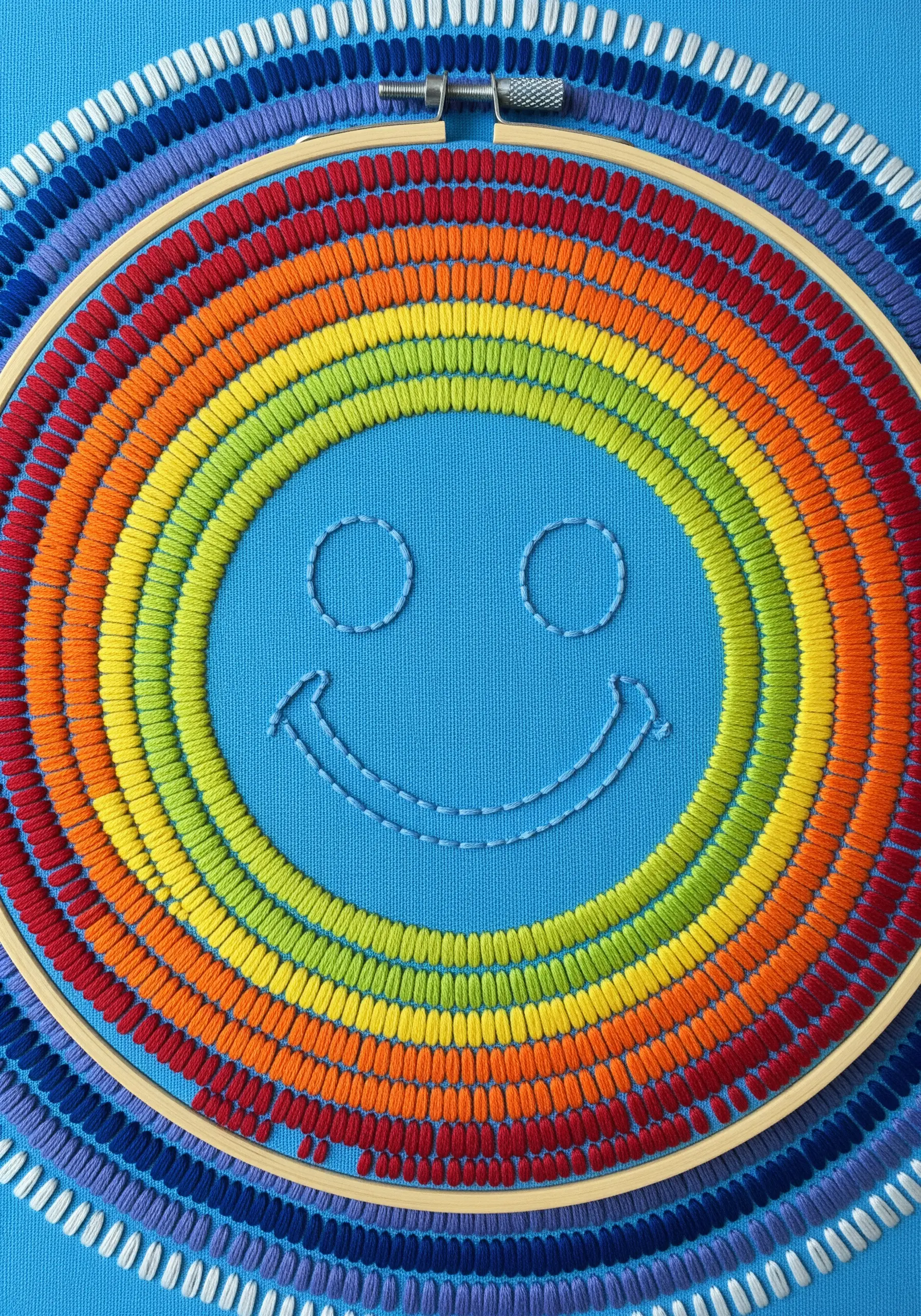 A simple smiley face in negative space, surrounded by vibrant concentric rings of rainbow satin stitch.