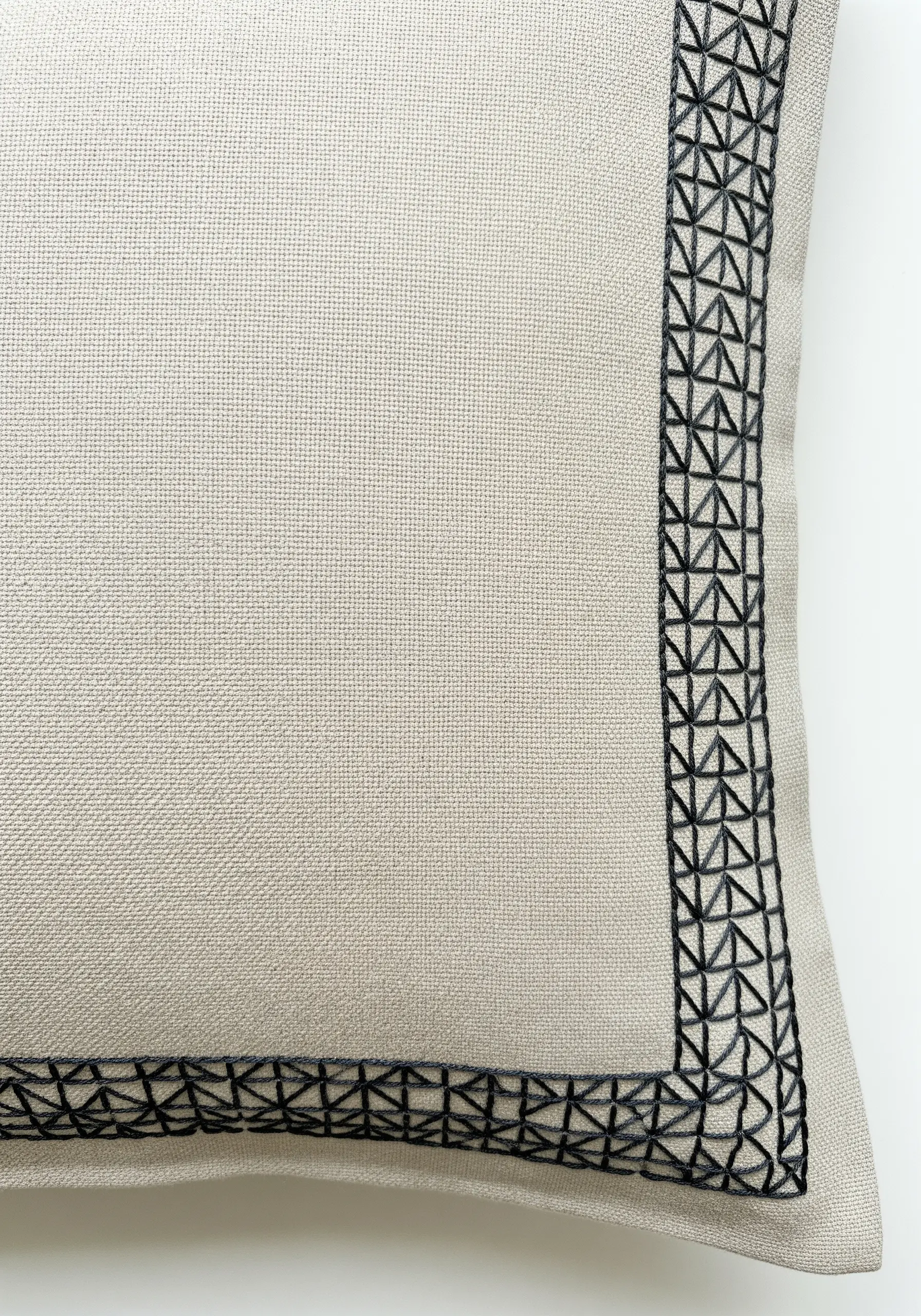 A close-up of a geometric border in black thread stitched along the edge of a beige pillowcase.