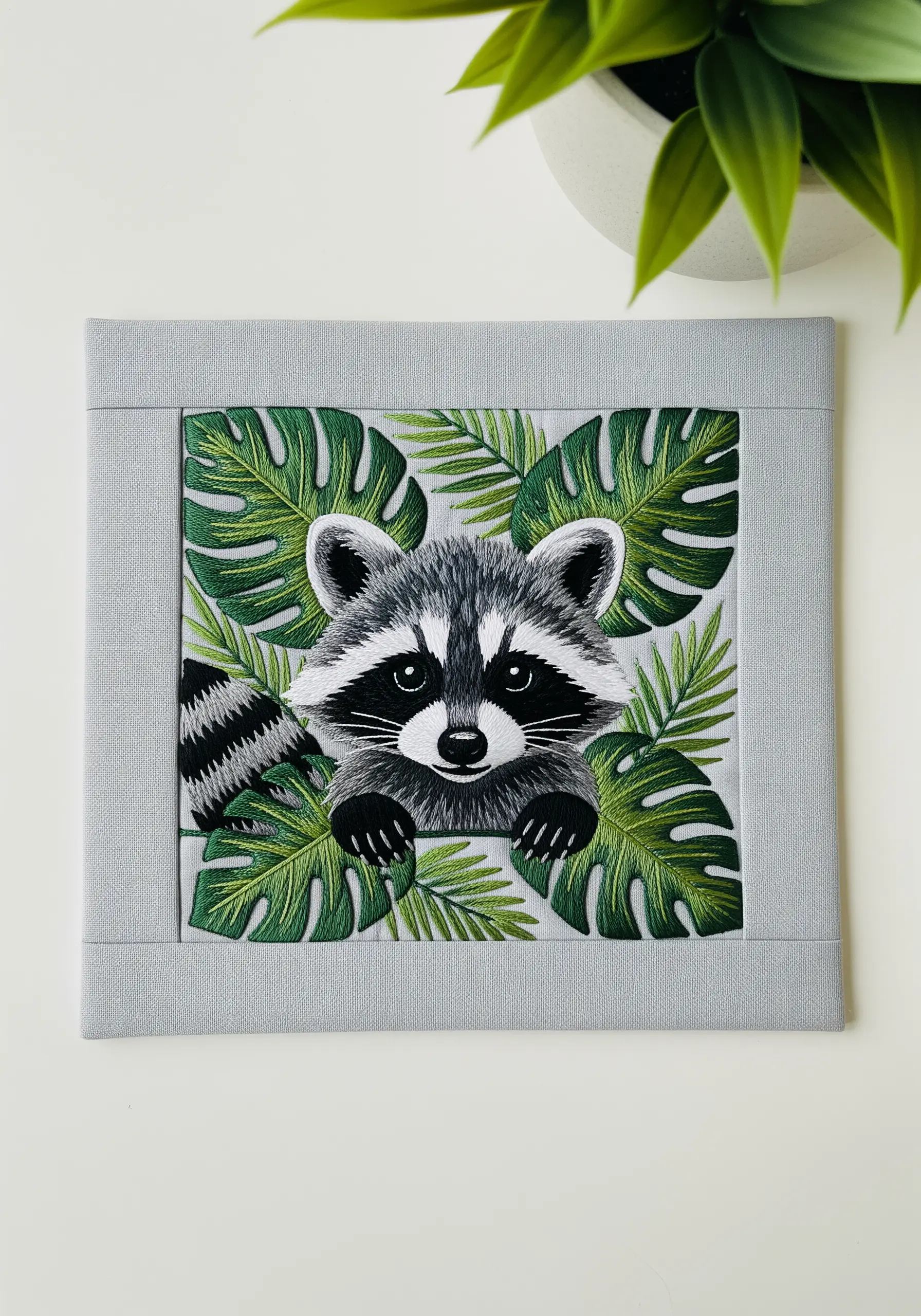 Embroidered raccoon face framed by lush, layered tropical leaves.