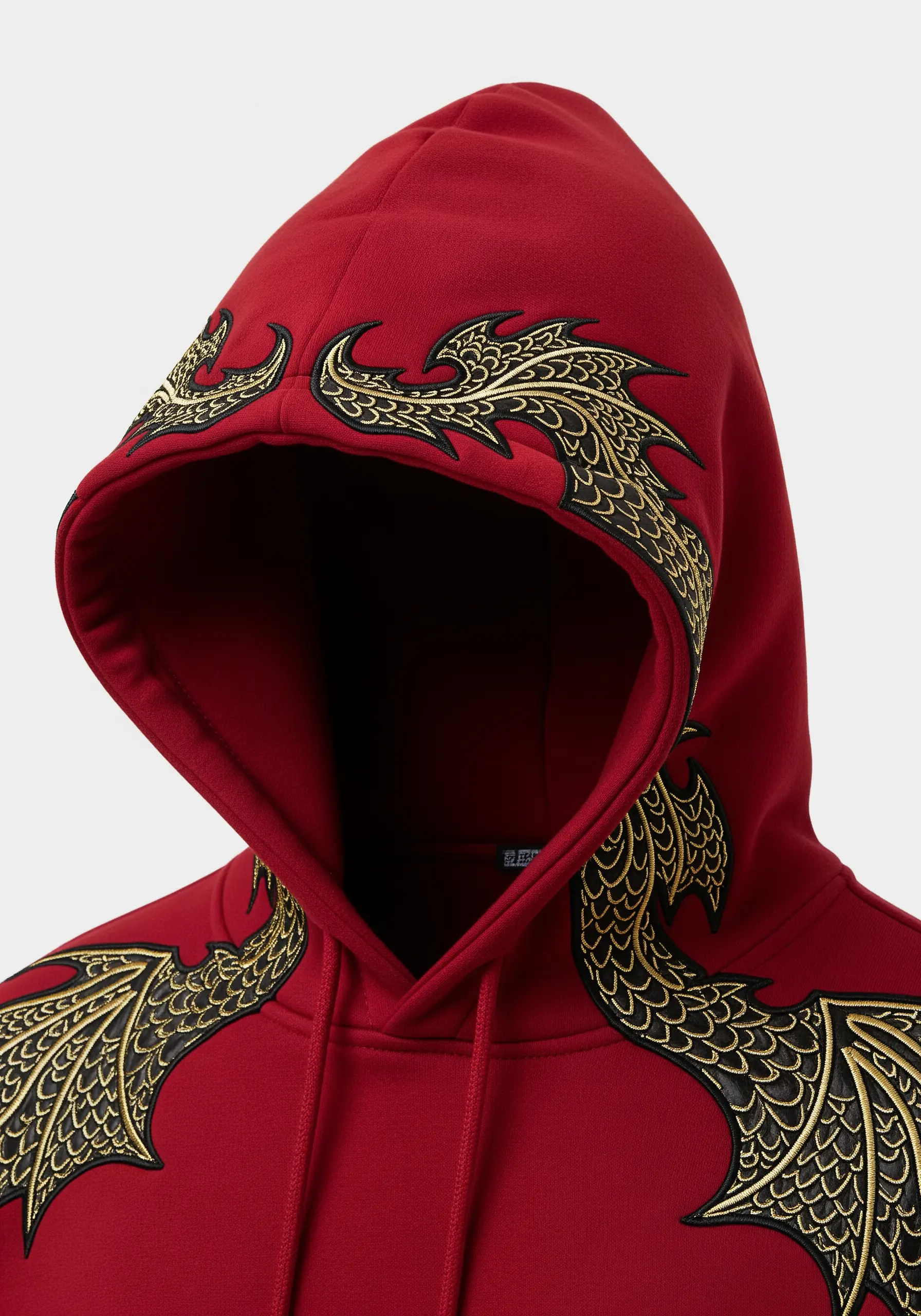 Ornate gold and black dragon wings embroidered along the edge of a red hoodie's hood.