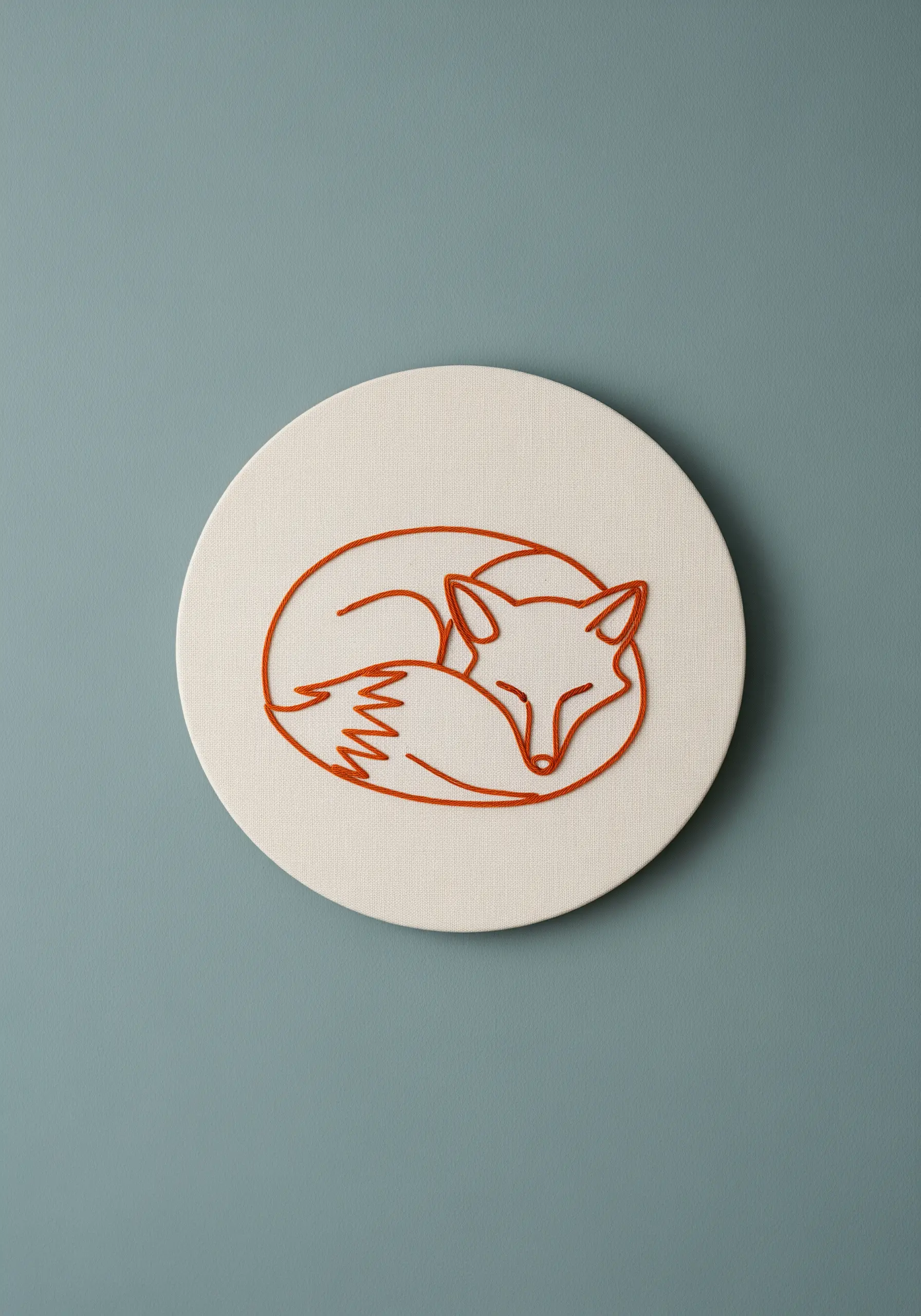 A minimalist sleeping fox embroidered in red-orange thread on a round, frameless canvas.