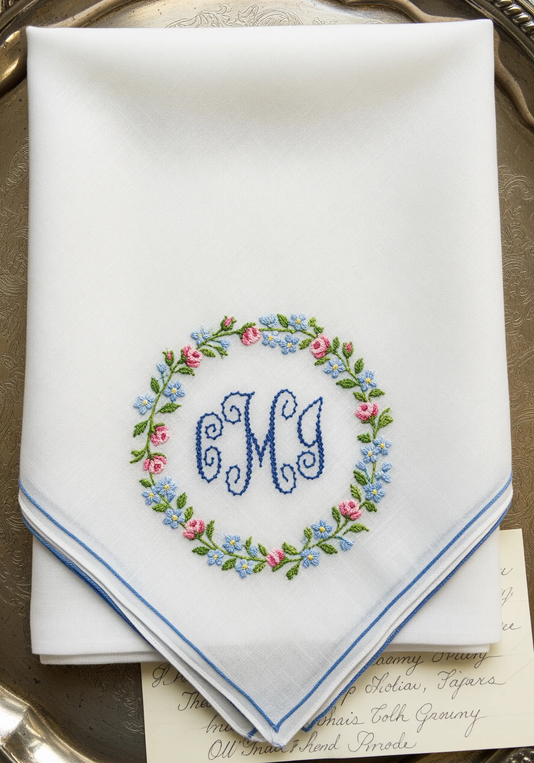 A classic 'M' monogram on a handkerchief, encircled by a delicate floral wreath.