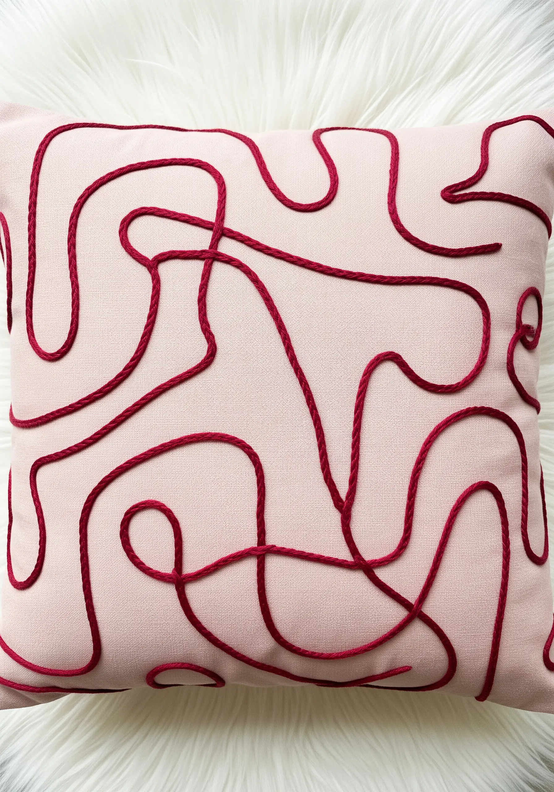 A free-form, meandering red line made from fabric tubing on a pale pink pillow.