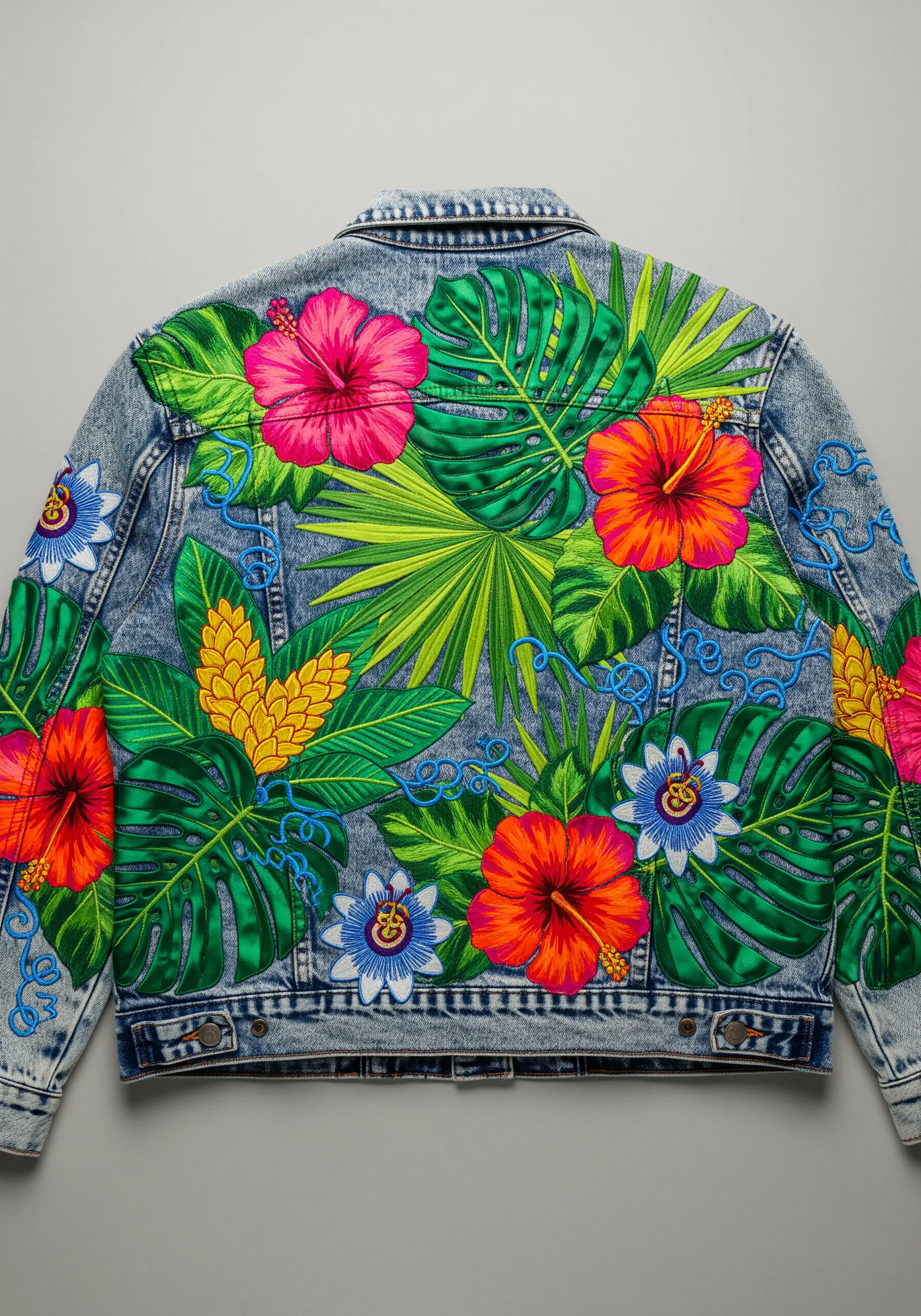 A vibrant, full-back embroidery of tropical flowers and leaves on a denim jacket.
