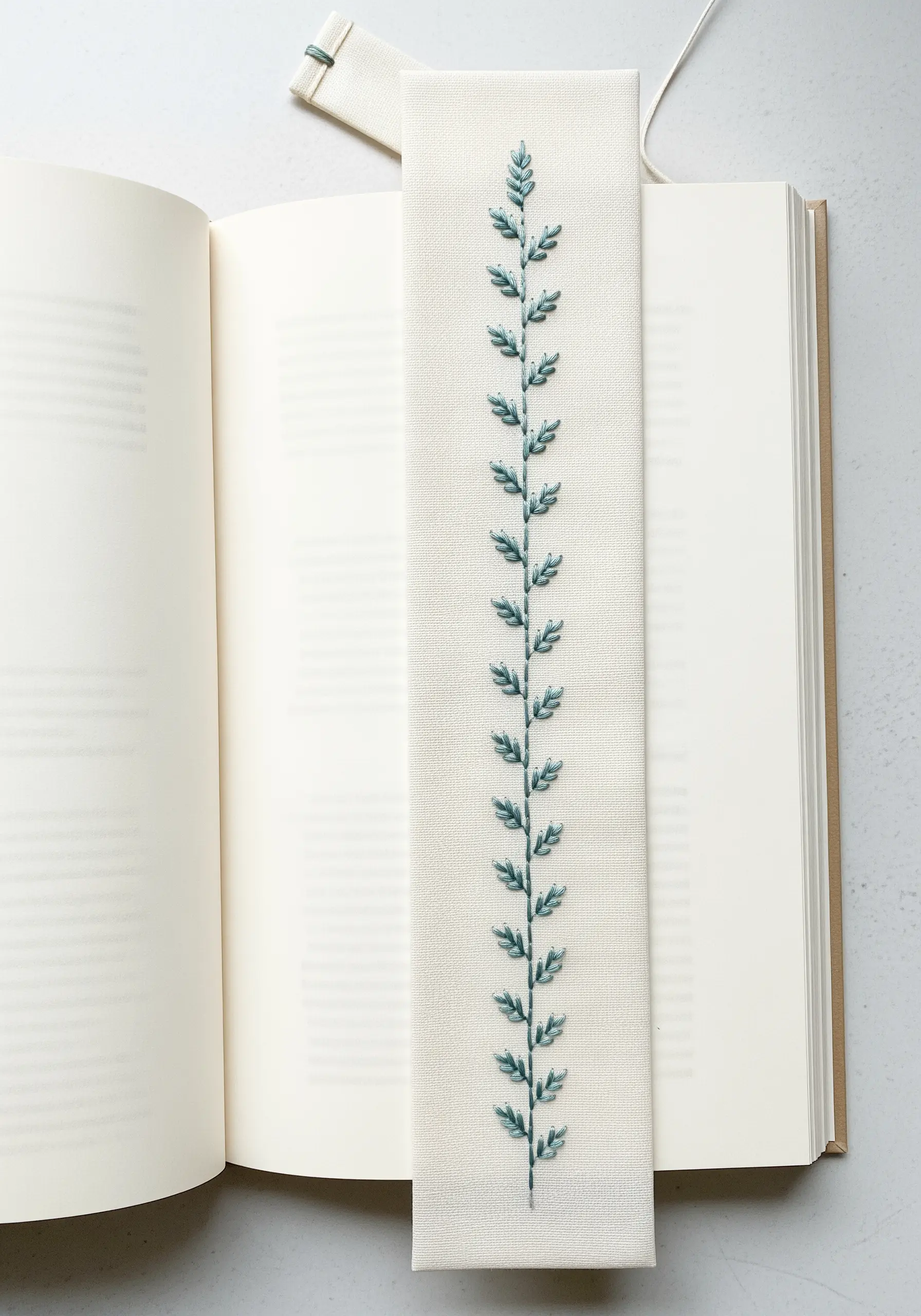 A handmade bookmark with a central vine embroidered using green variegated fly stitches.