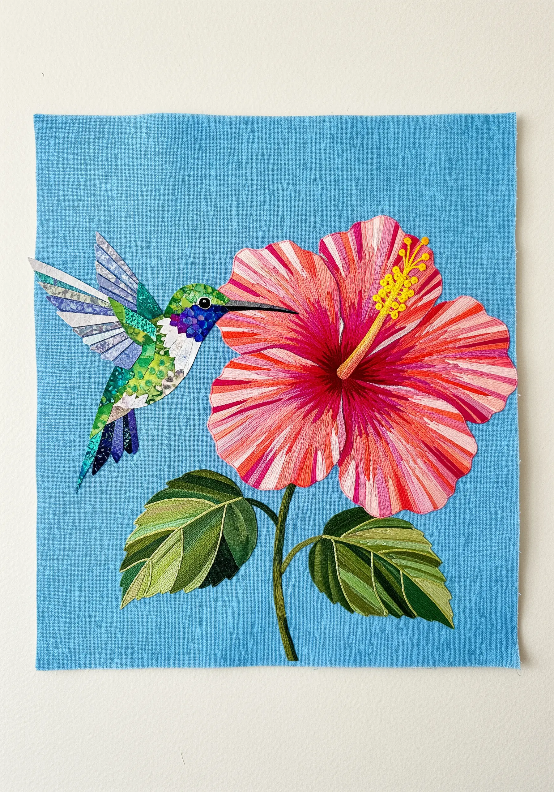 Hummingbird and hibiscus made with fabric appliqué and detailed long-and-short stitch embroidery.