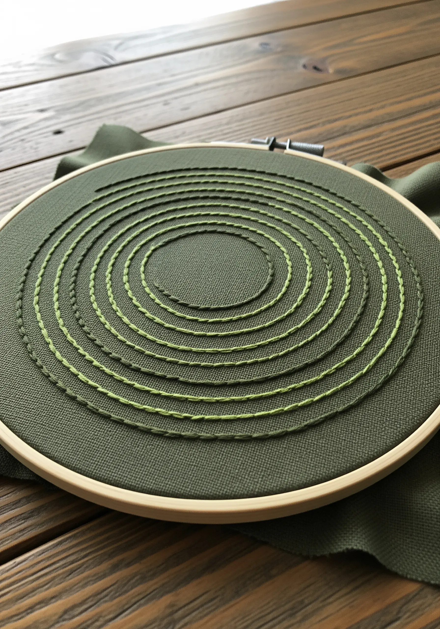 Concentric circles in green running stitch on dark olive fabric, creating a subtle gradient.