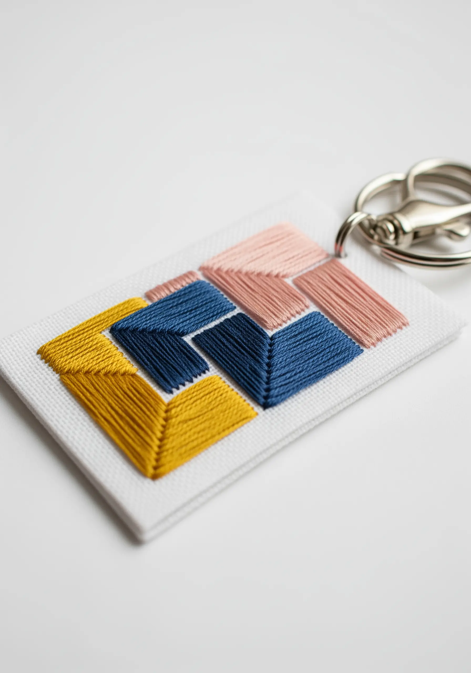 Geometric satin stitch blocks in yellow, blue, and pink on a white keychain