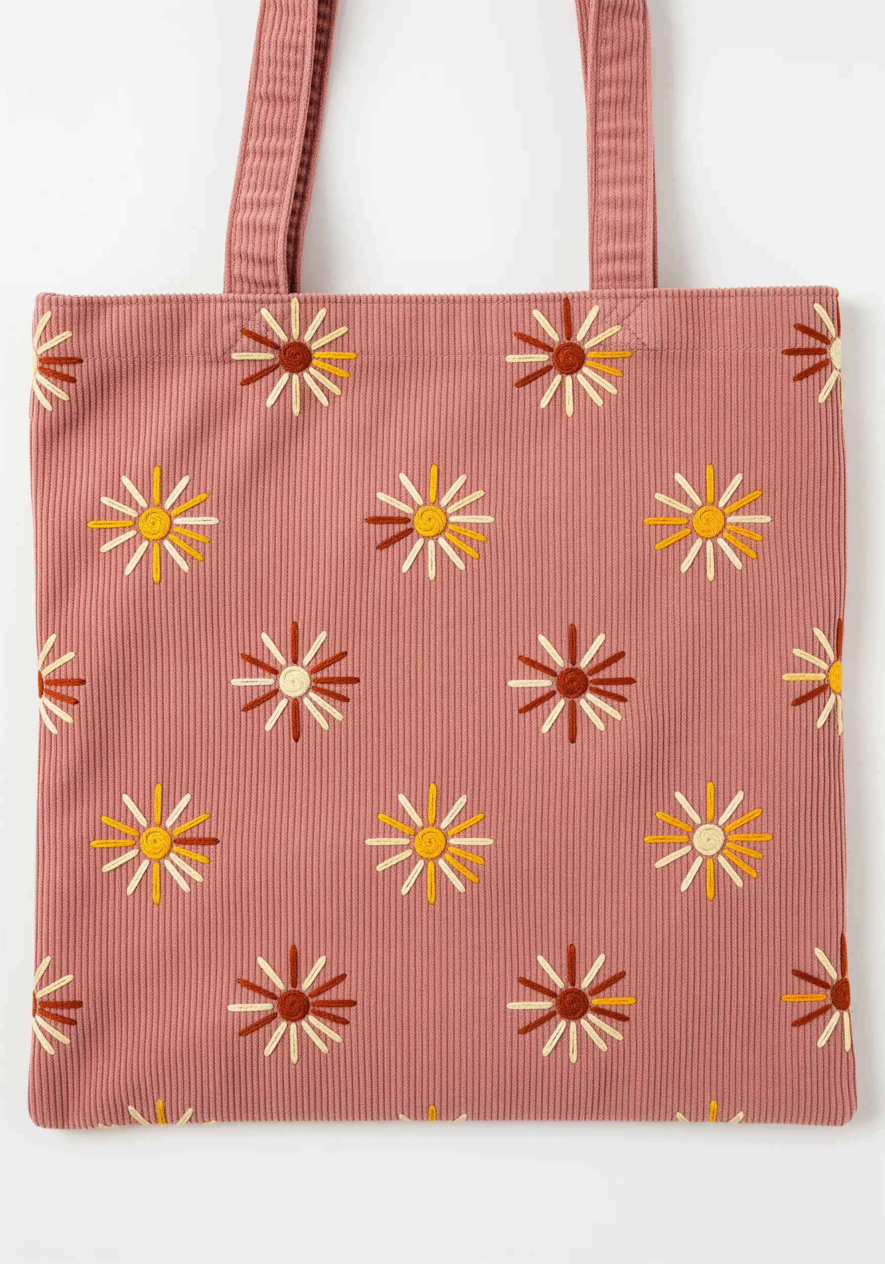 A repeating pattern of stylized sunburst flowers on a pink corduroy tote bag.