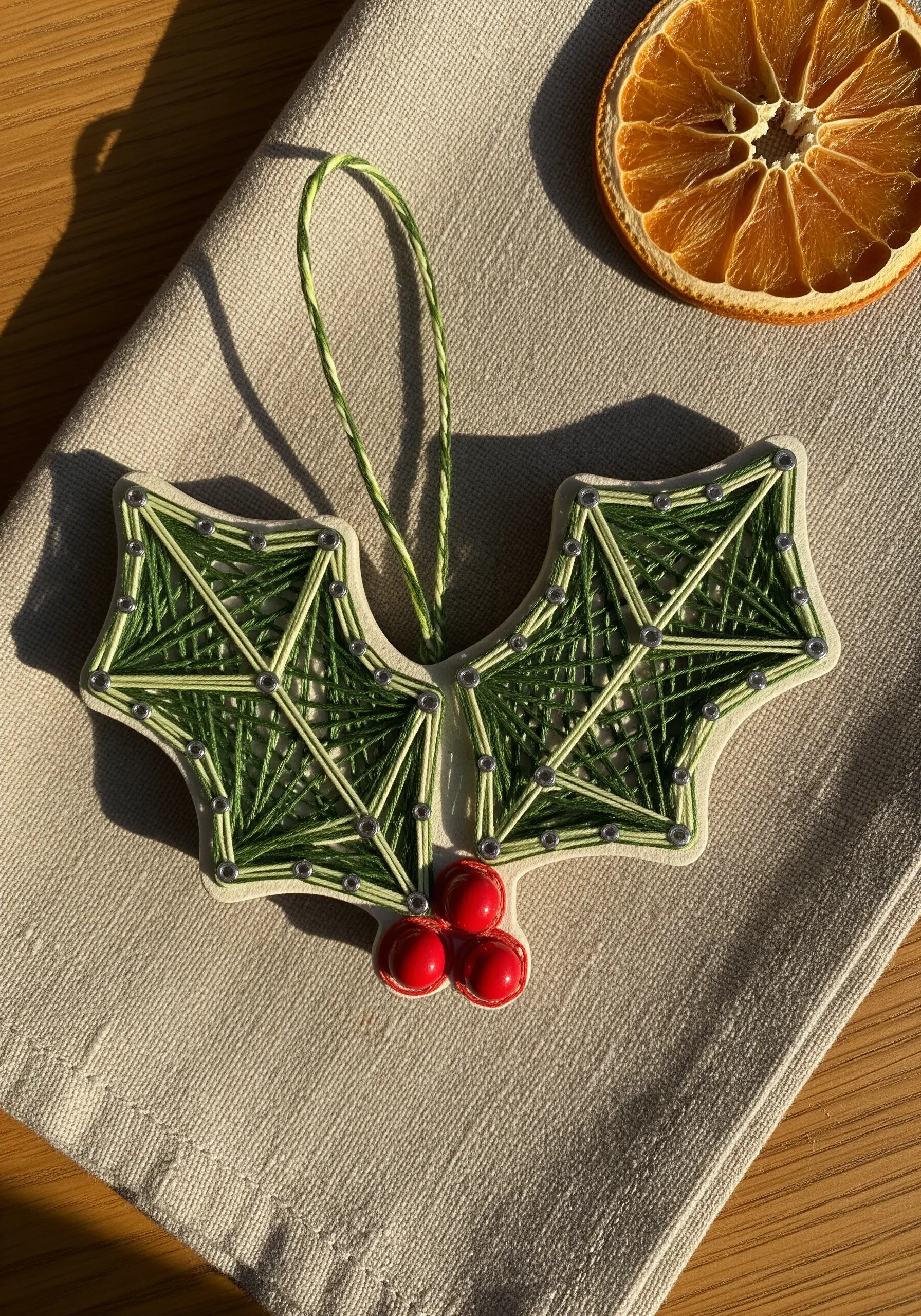 Geometric string art holly leaves with bead berries on a linen background.