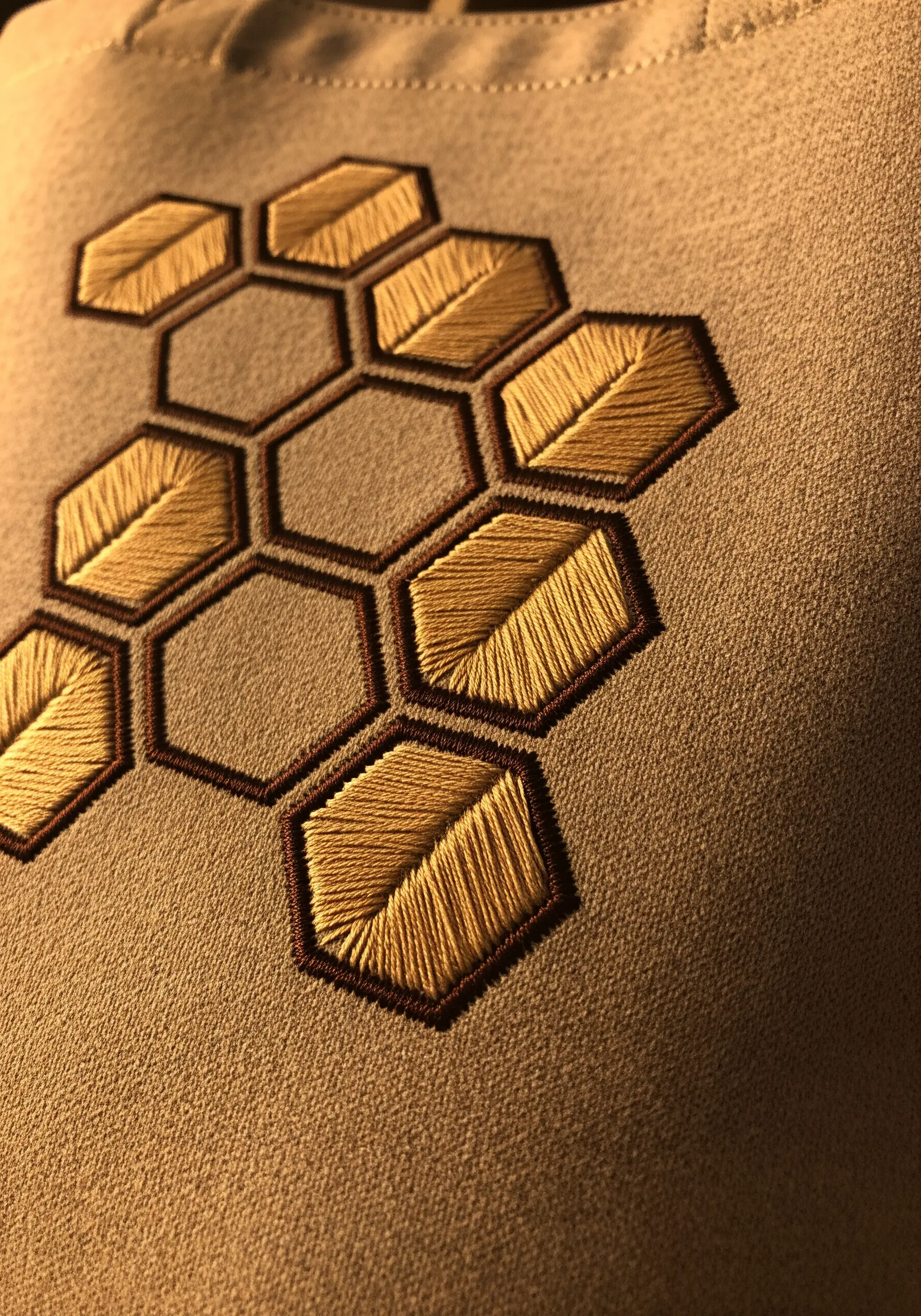 A honeycomb pattern embroidered in gold and brown, with some cells filled with leaf textures.