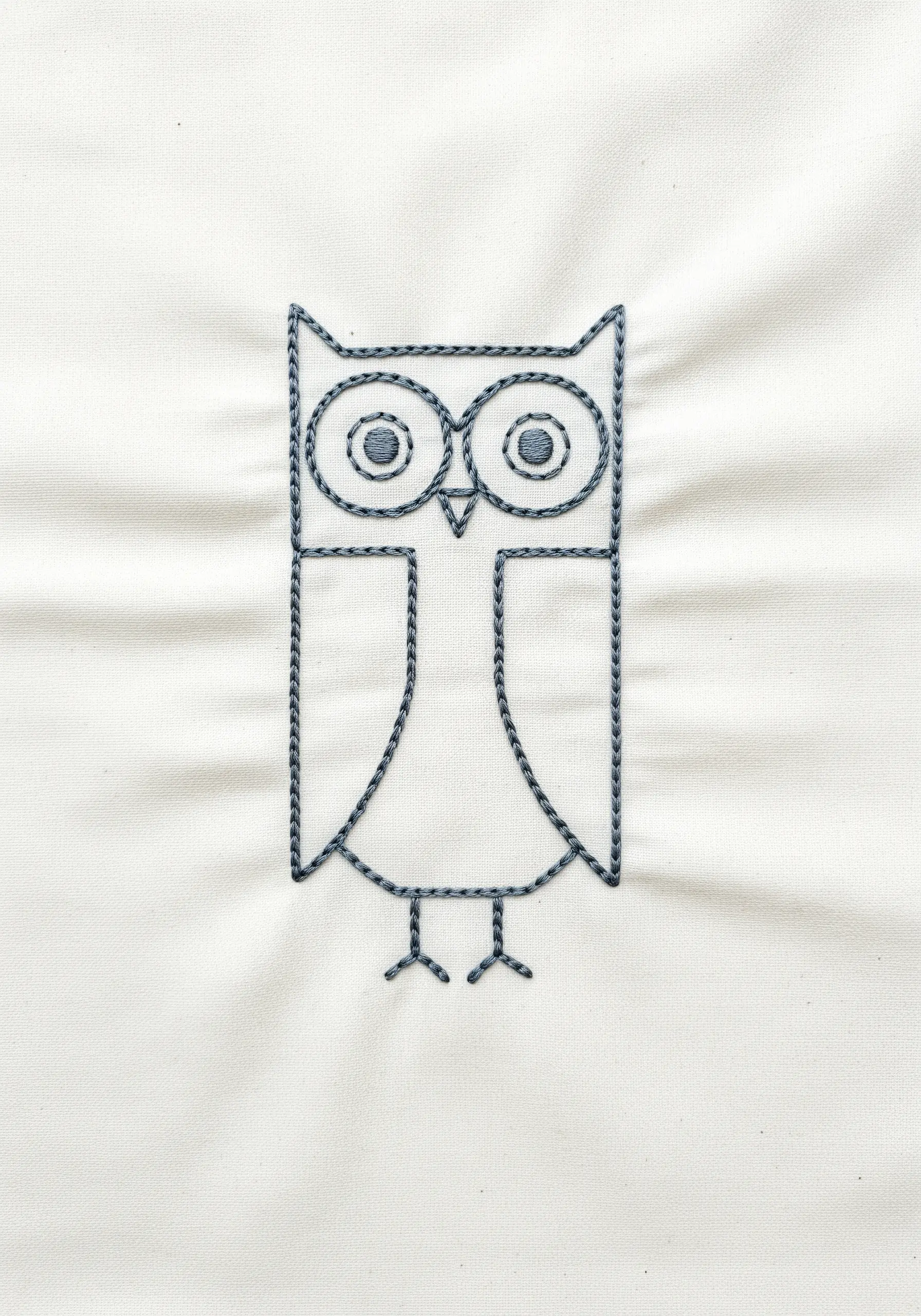 Geometric owl embroidery using dark grey chain stitch on white fabric