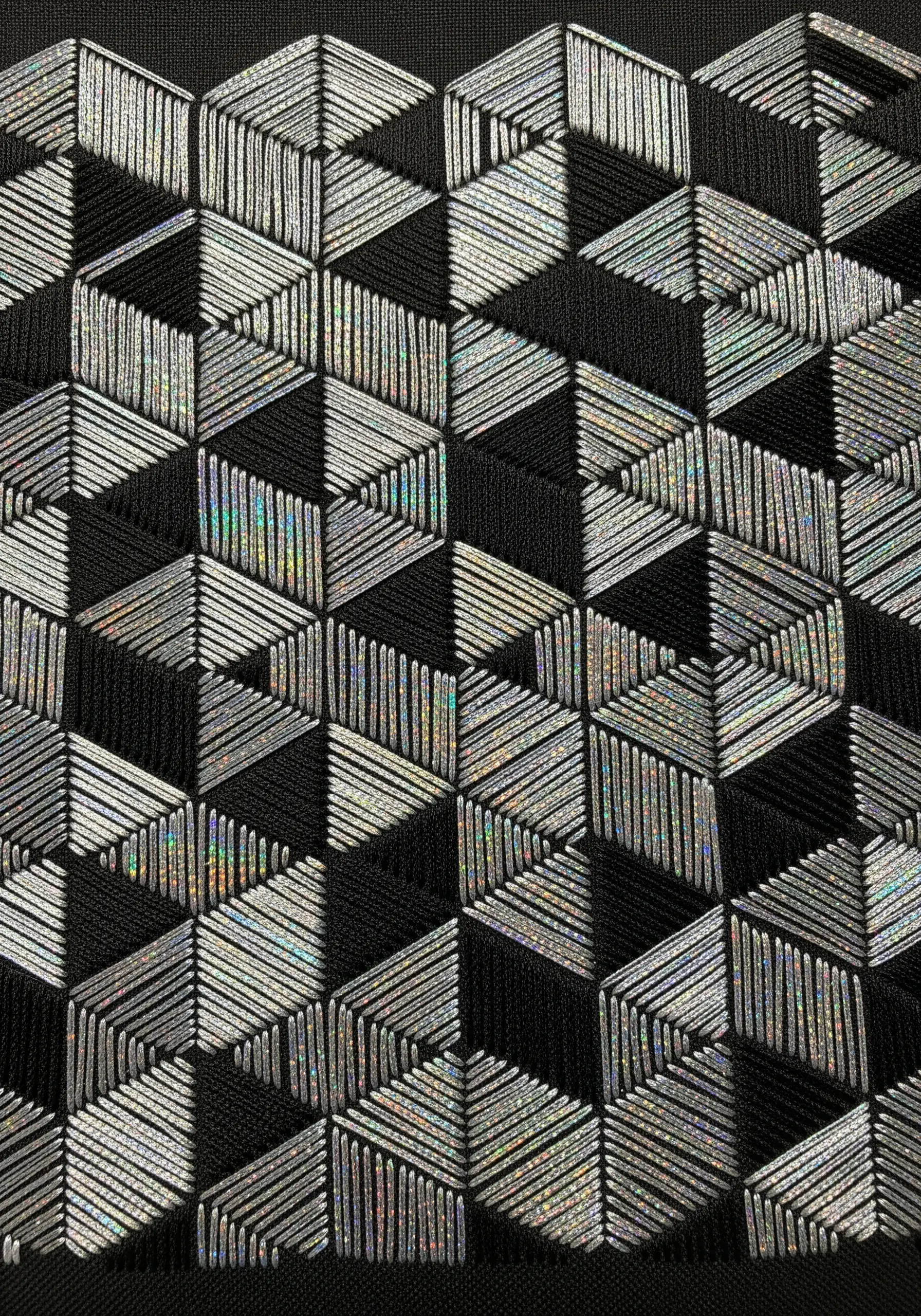 A geometric pattern of 3D cubes stitched with holographic and black thread.