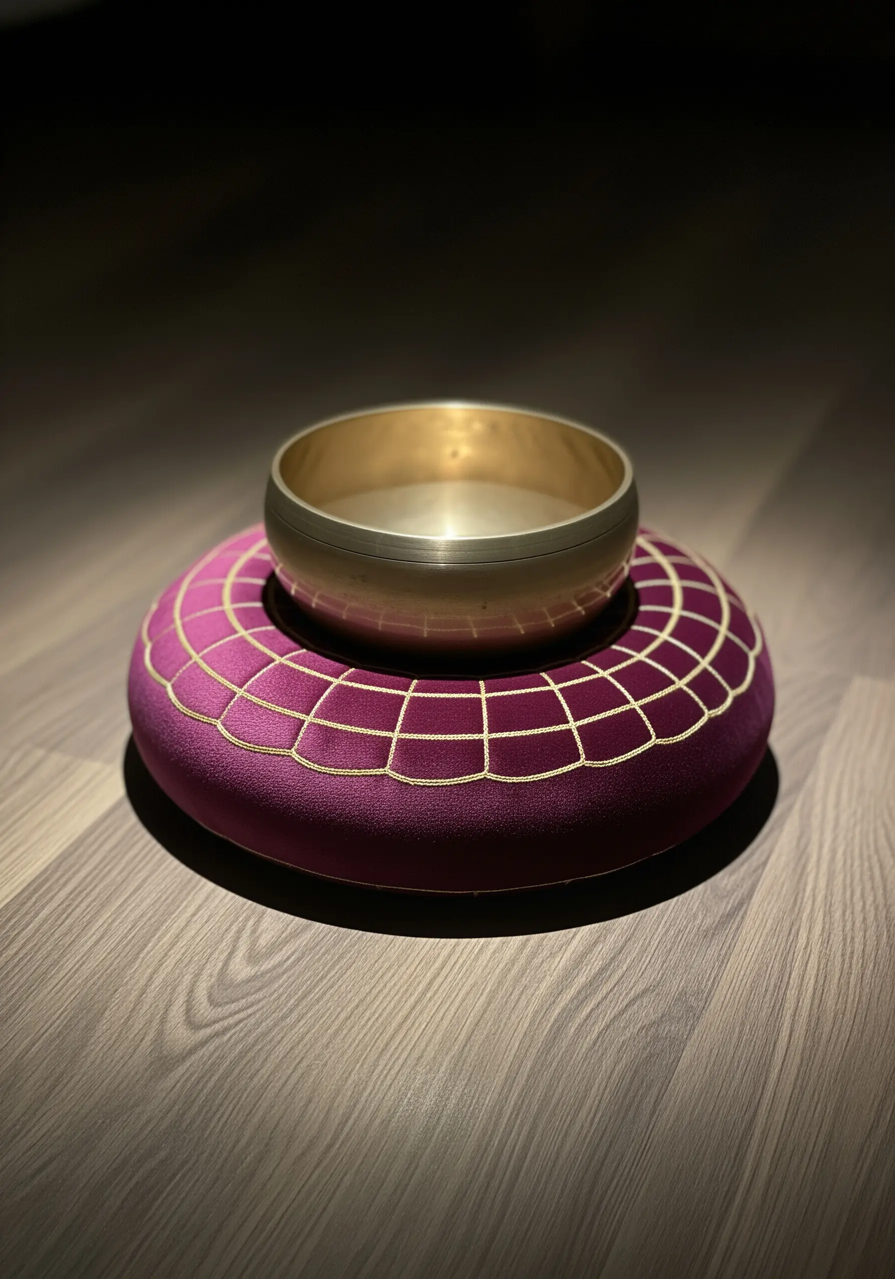 A golden singing bowl resting on a plush purple cushion with a gold embroidered grid pattern.