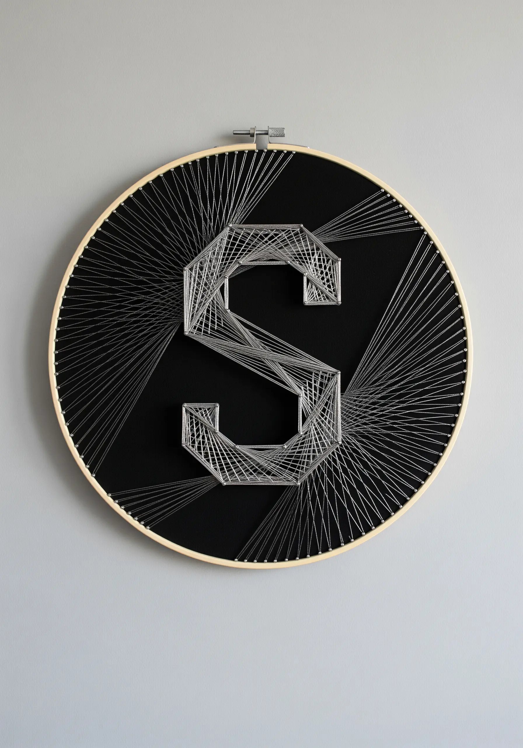 A single silver metallic thread creating a geometric monogram on a black background.