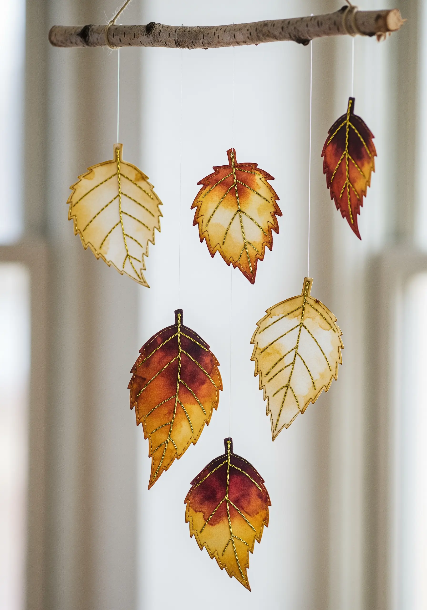Hanging mobile with watercolor paper leaves detailed with gold metallic thread veins.