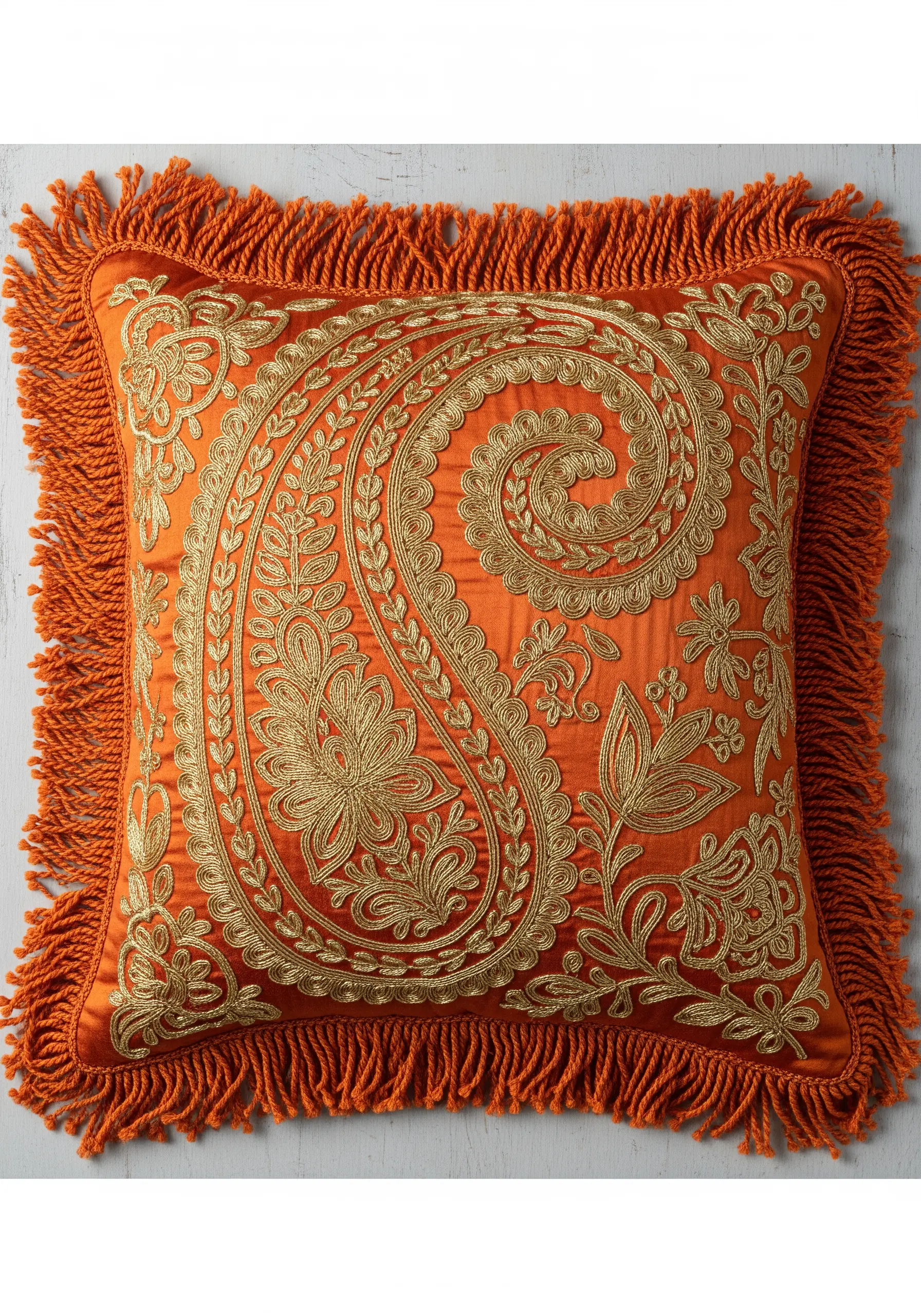Ornate gold paisley embroidery on a vibrant orange silk pillow with a thick fringe.
