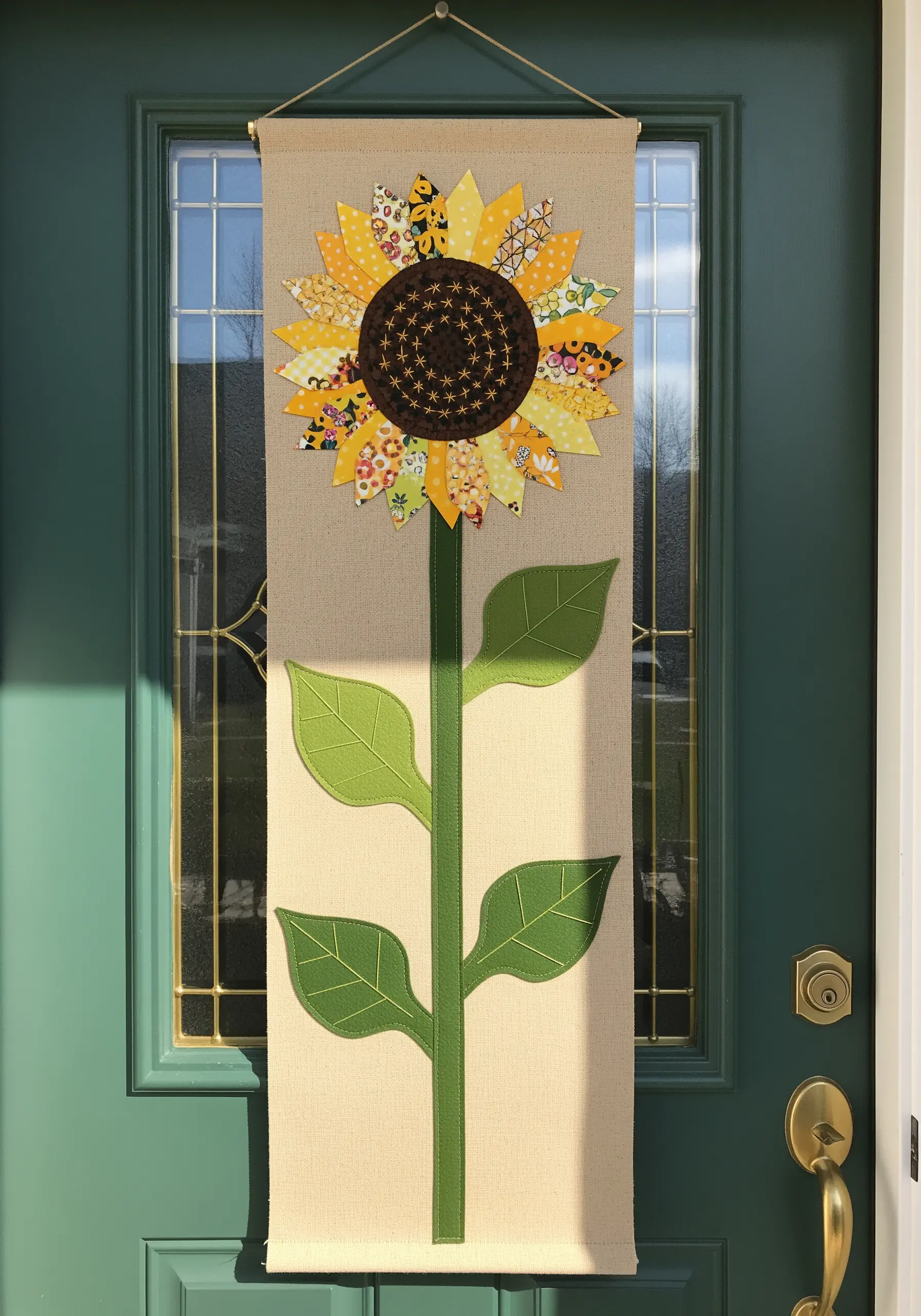 A large wall banner of a sunflower made from multiple patterned yellow fabric scraps.