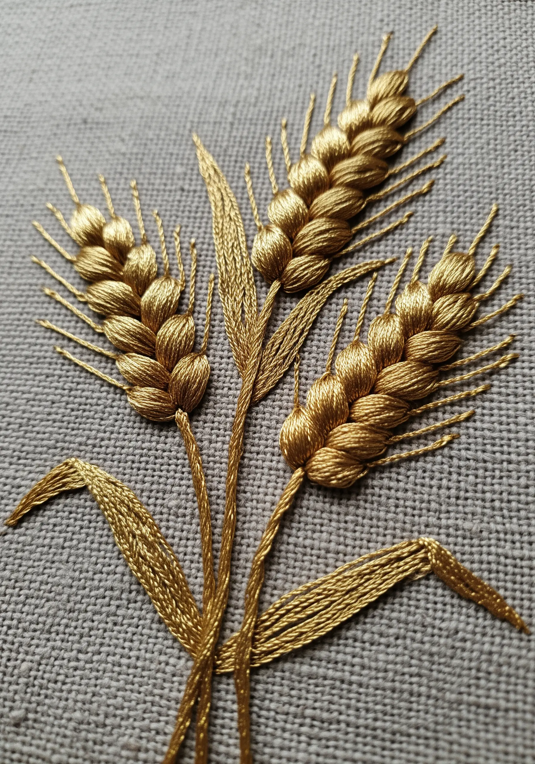 Gold thread embroidery of wheat stalks on grey linen