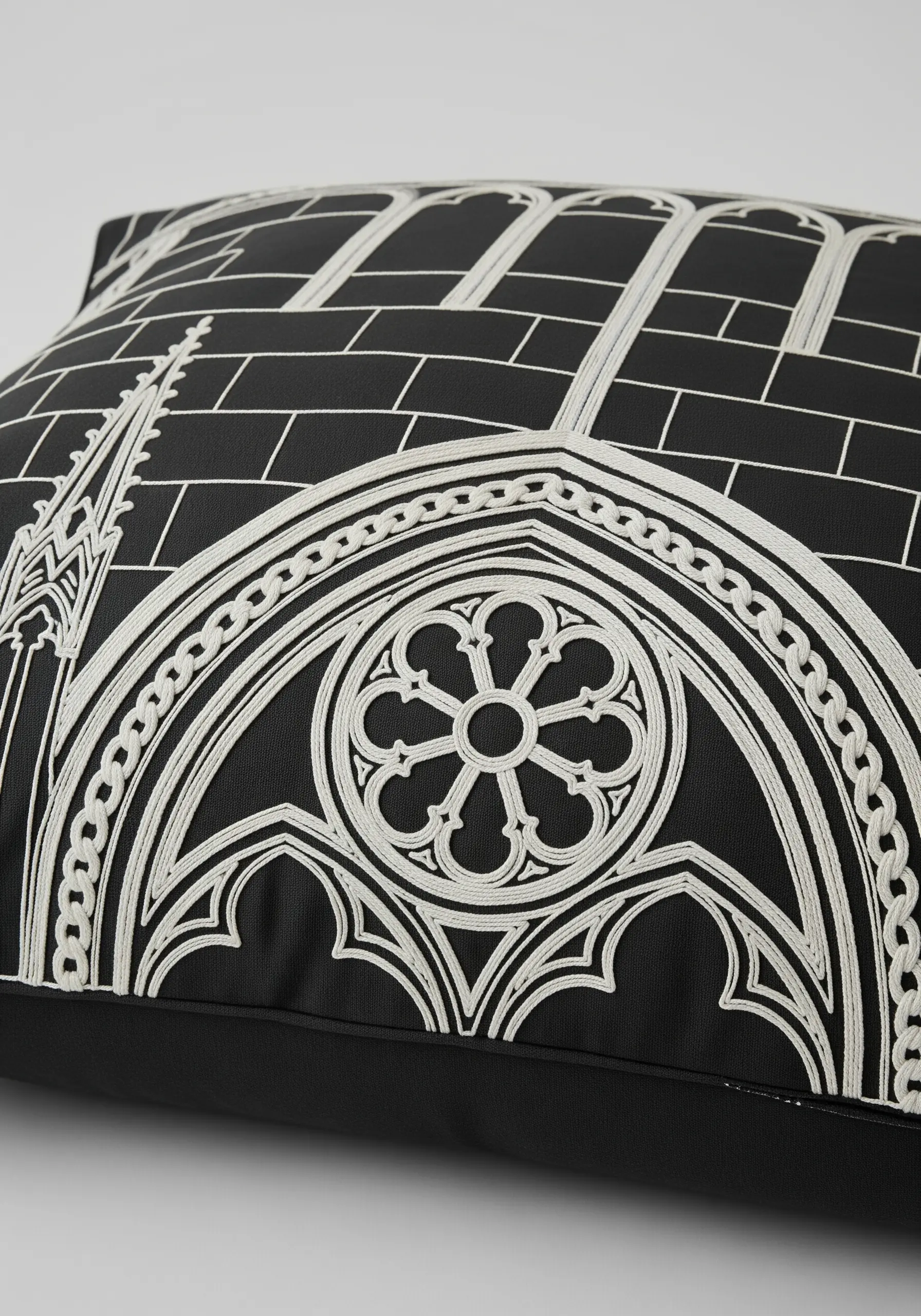 The white-on-black embroidered outline of a gothic cathedral window on a black cushion.