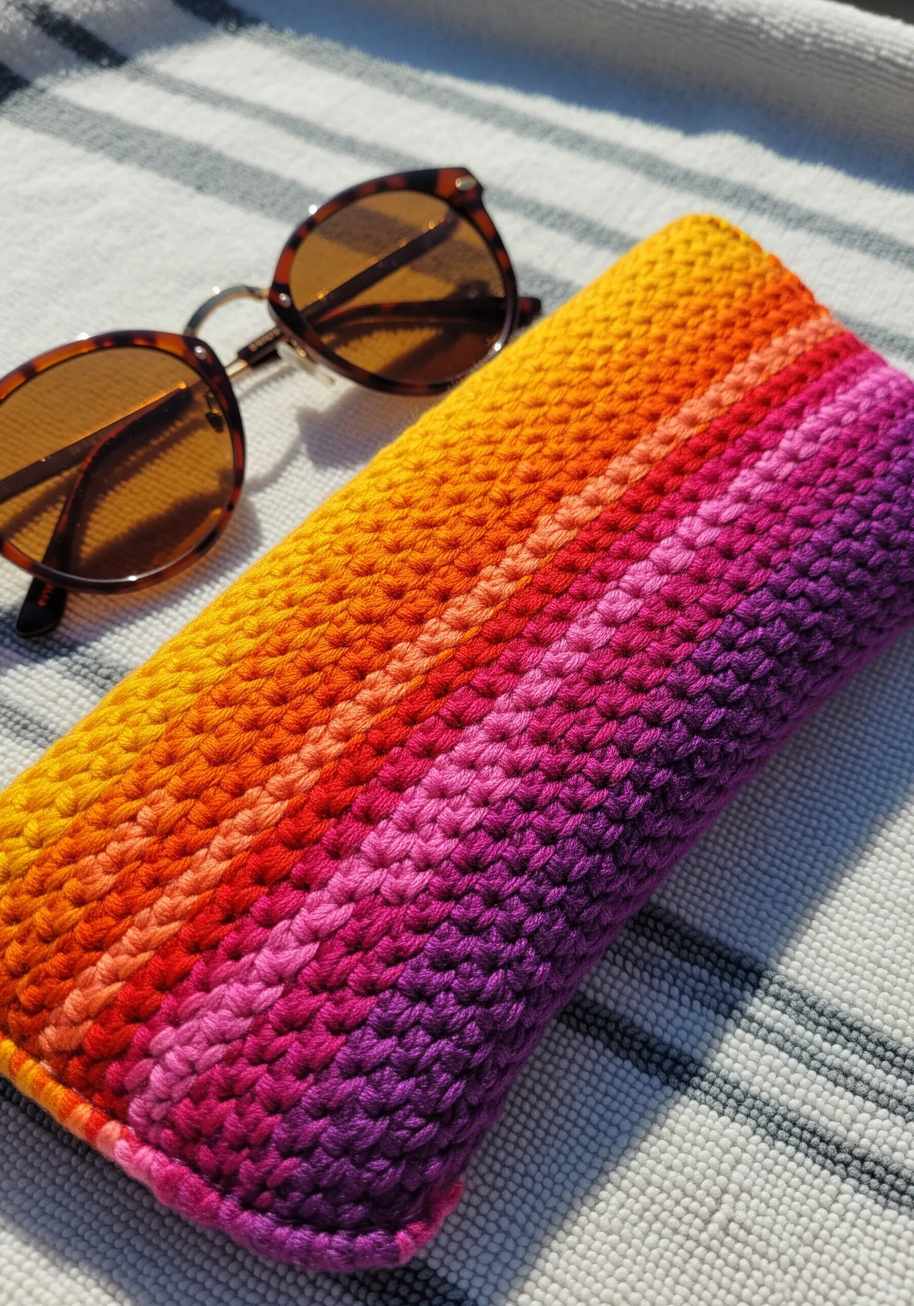 A brightly colored, crocheted sunglasses case with a warm-to-cool gradient pattern.