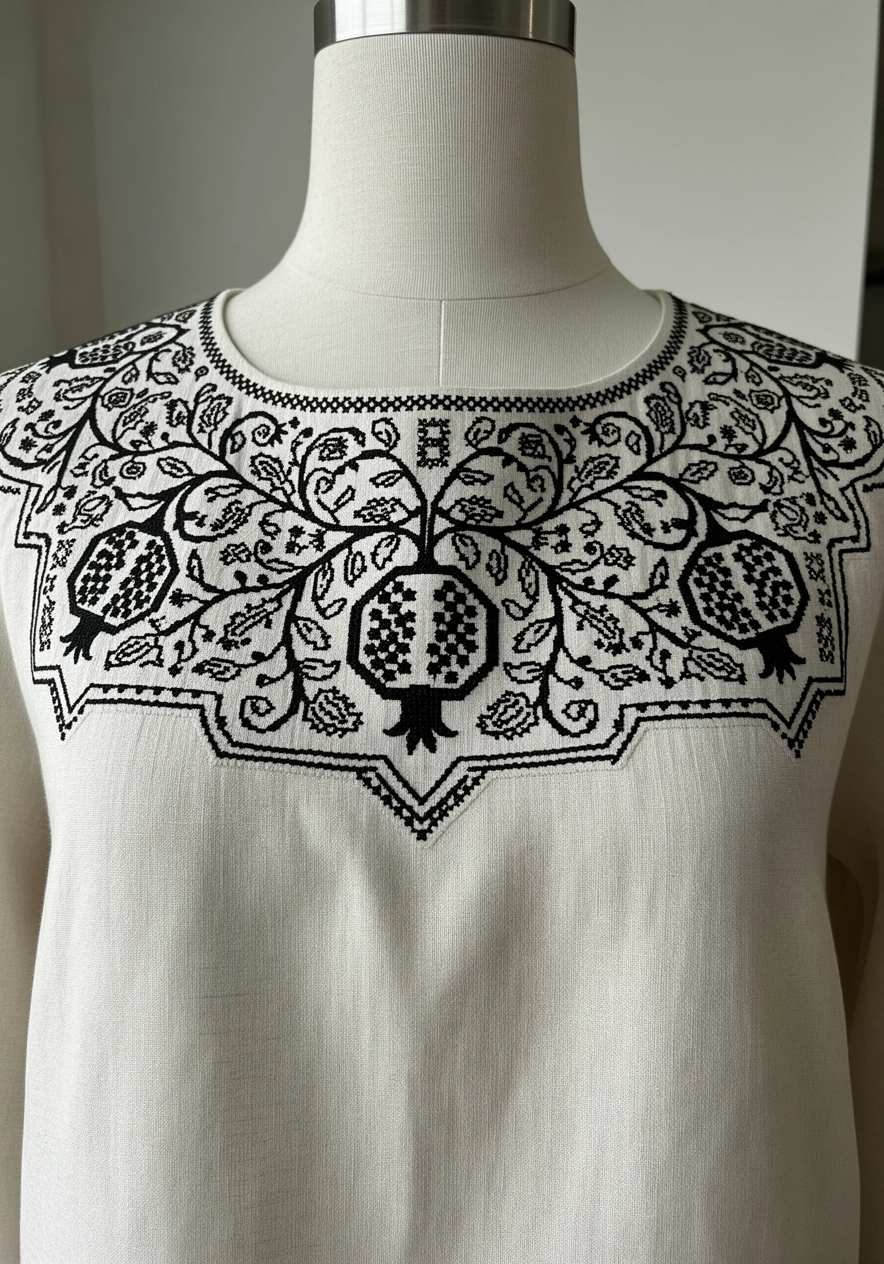 A blackwork yoke design with pomegranates and leaves using geometric fill patterns.