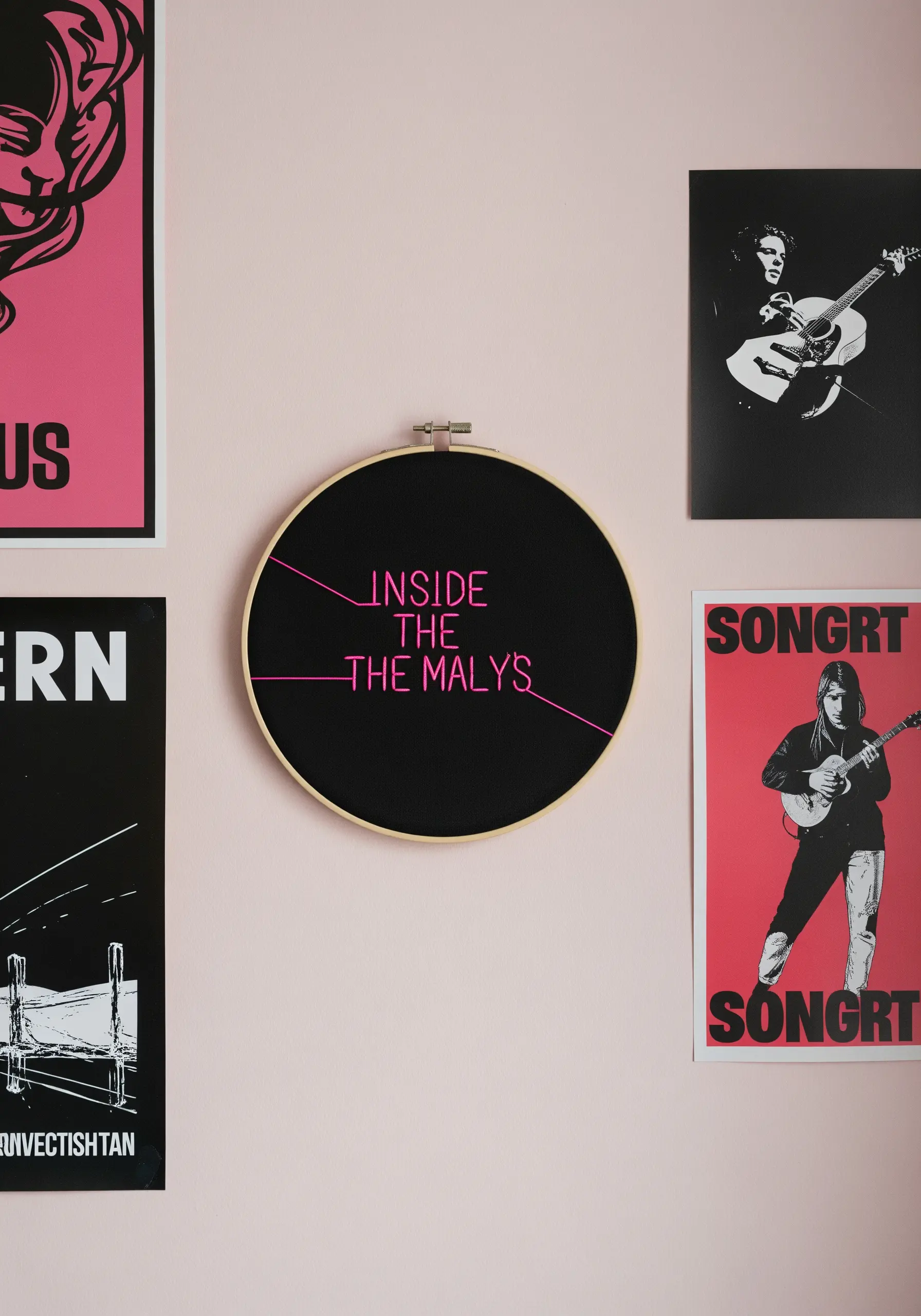 An embroidery hoop with minimalist pink text and lines on a black background.
