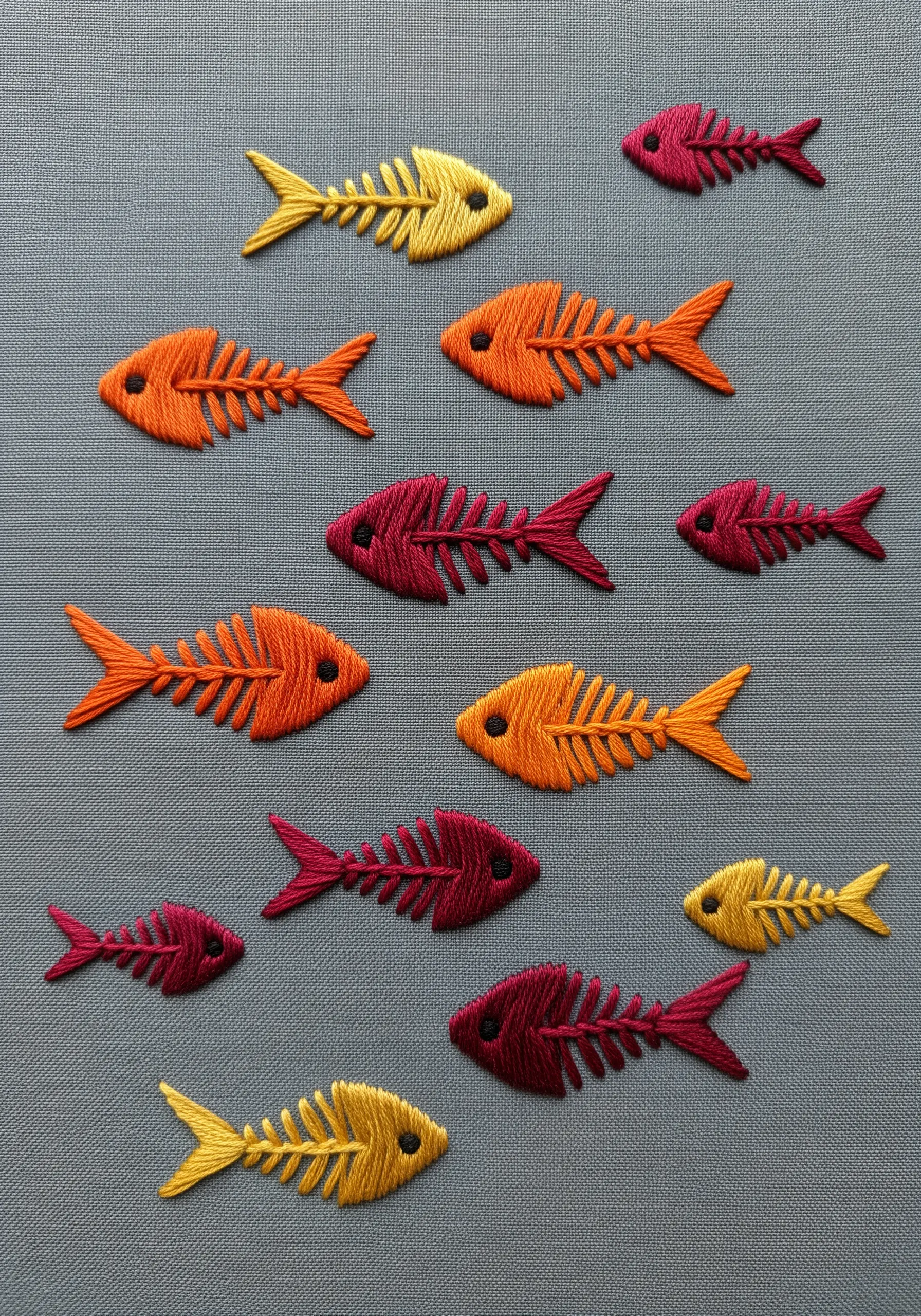 A pattern of repeating fish skeletons embroidered in warm tones of yellow, orange, and maroon.