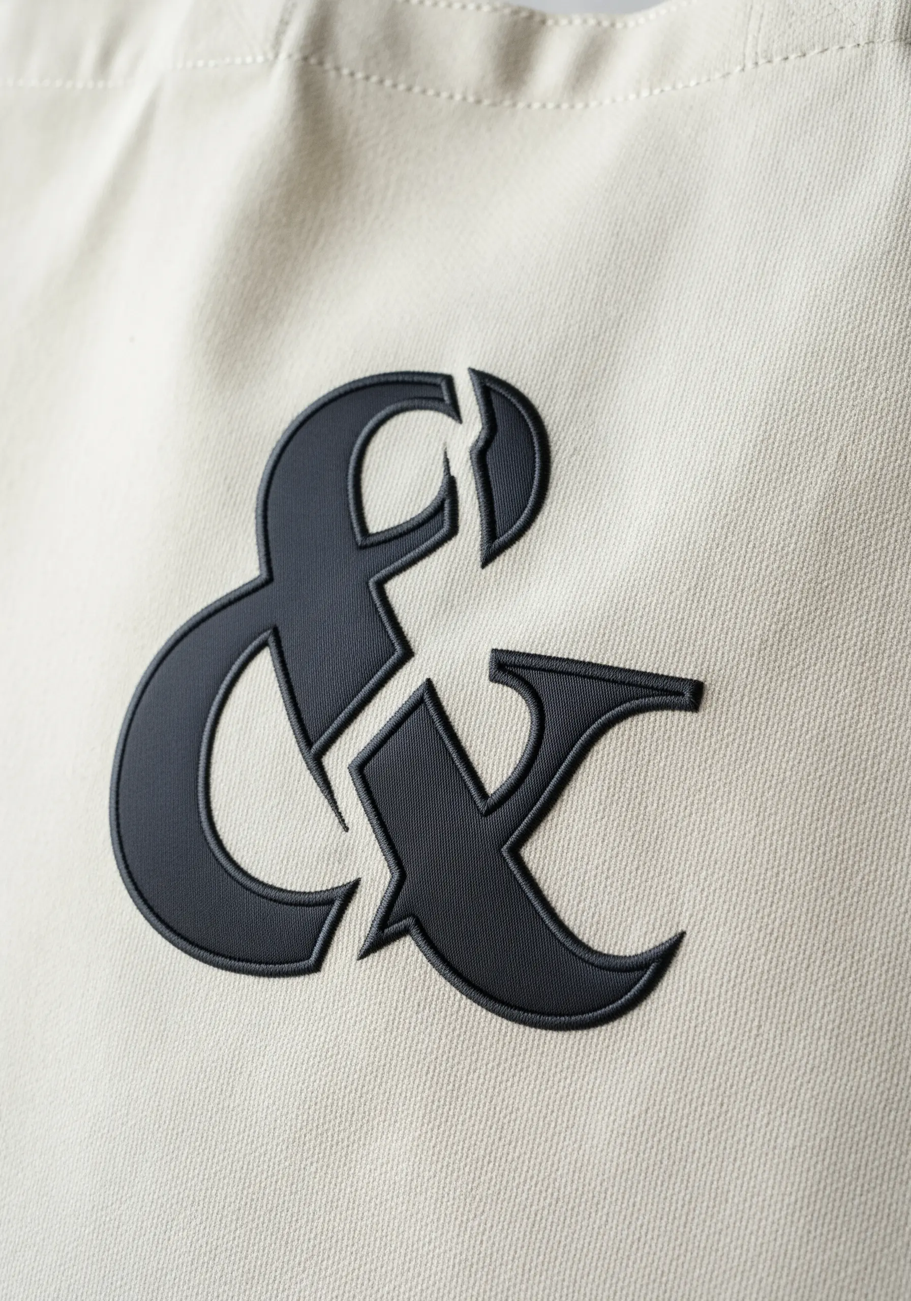 A close-up of a satin-stitched black ampersand with a split detail on a beige tote.