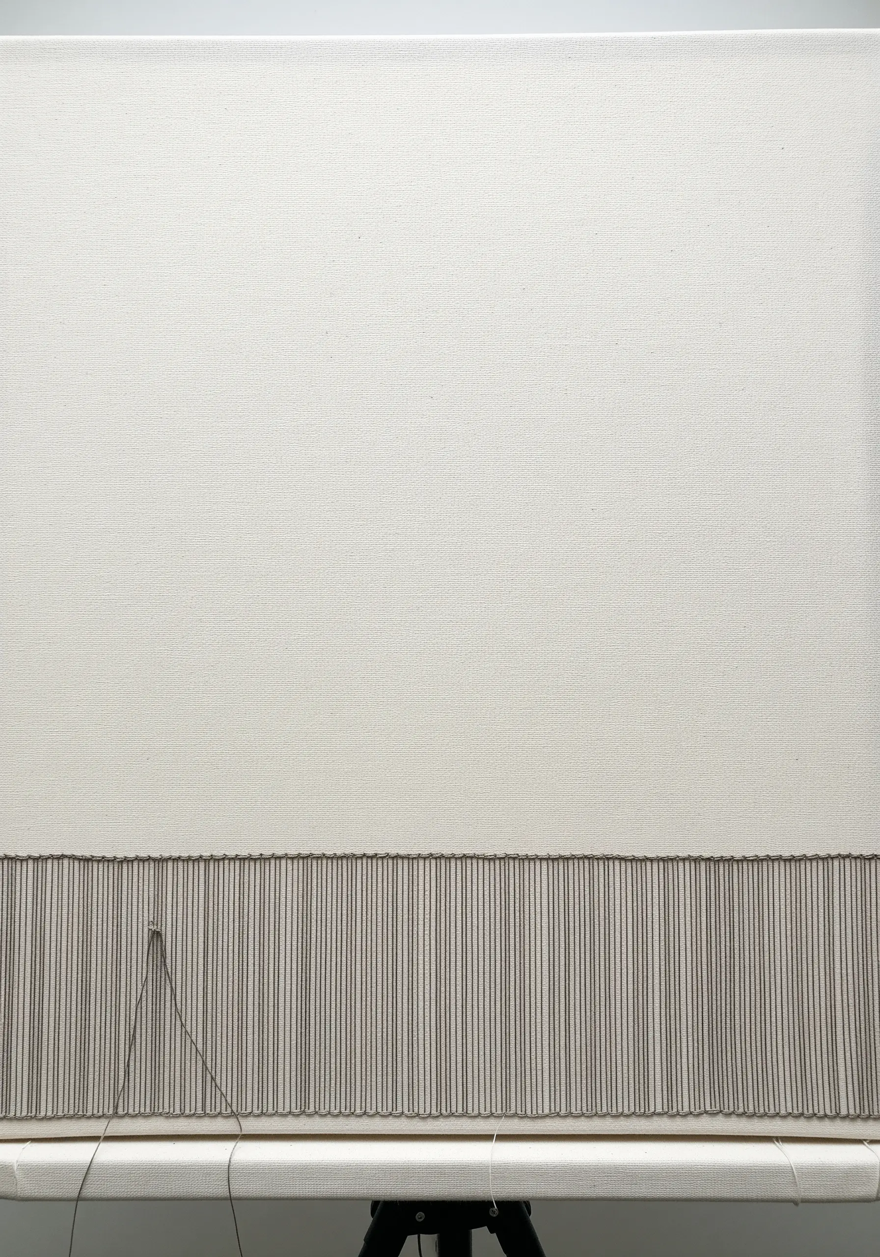 A dense band of vertical stitches along the bottom edge of a large, empty canvas.