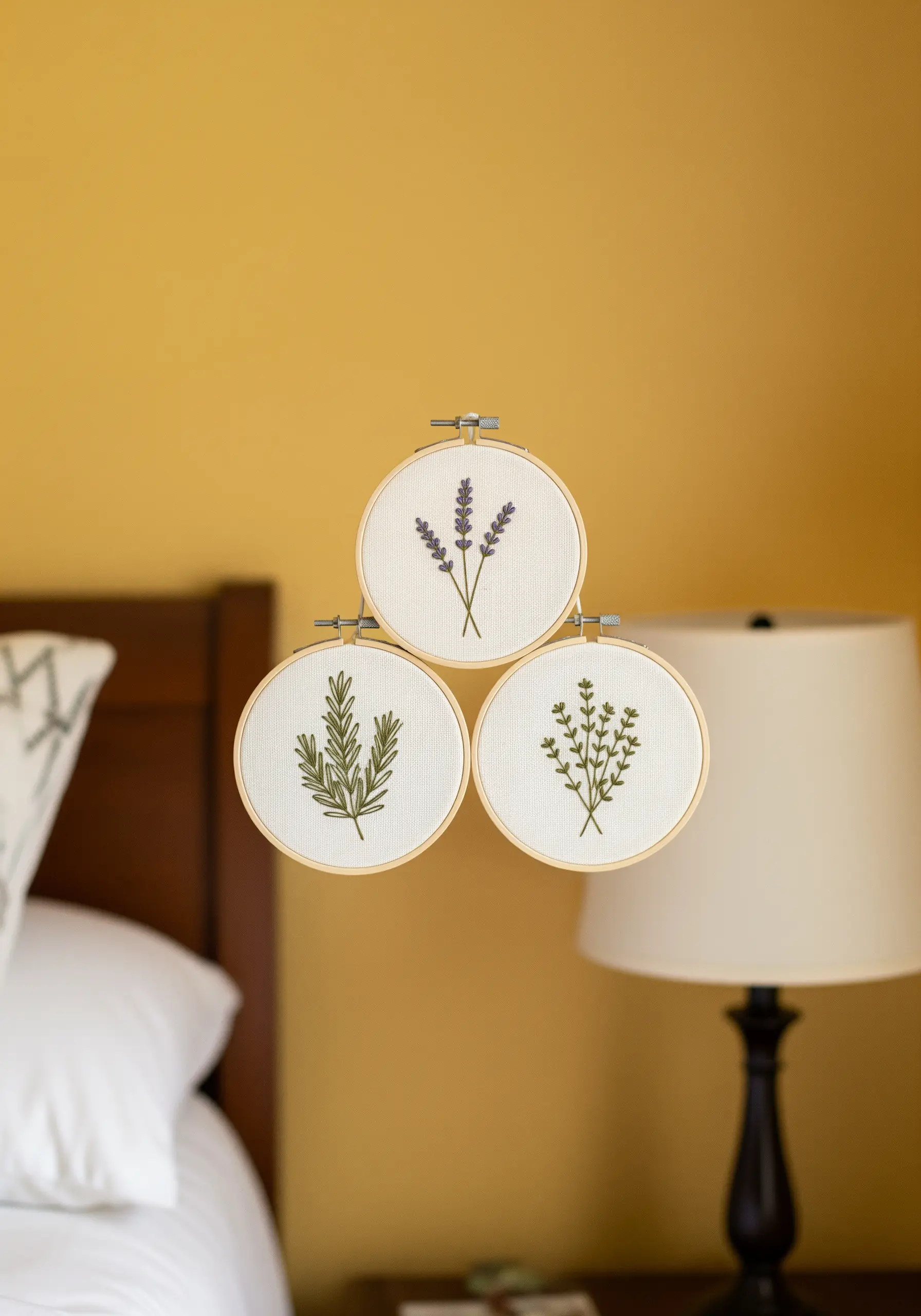 A trio of small embroidery hoops with lavender, rosemary, and another herb, clustered together.