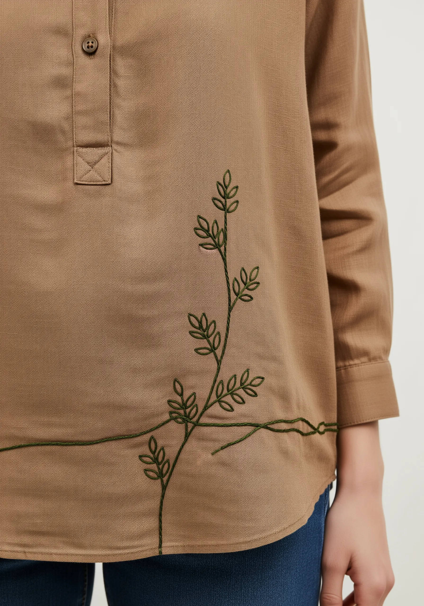 A delicate green vine with small leaves embroidered across the front of a brown linen shirt.