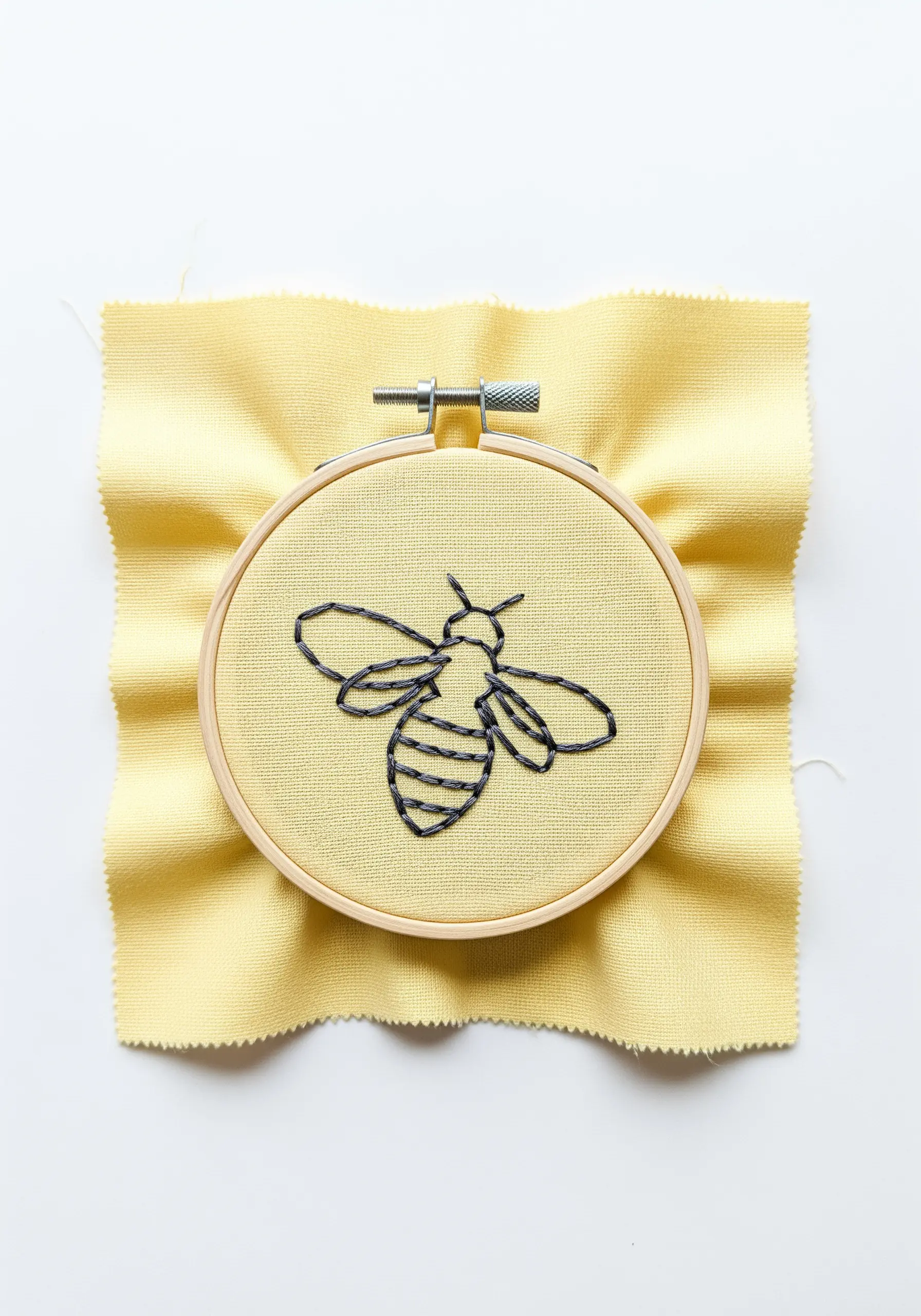 A minimalist bee outline created with black backstitch on yellow fabric.