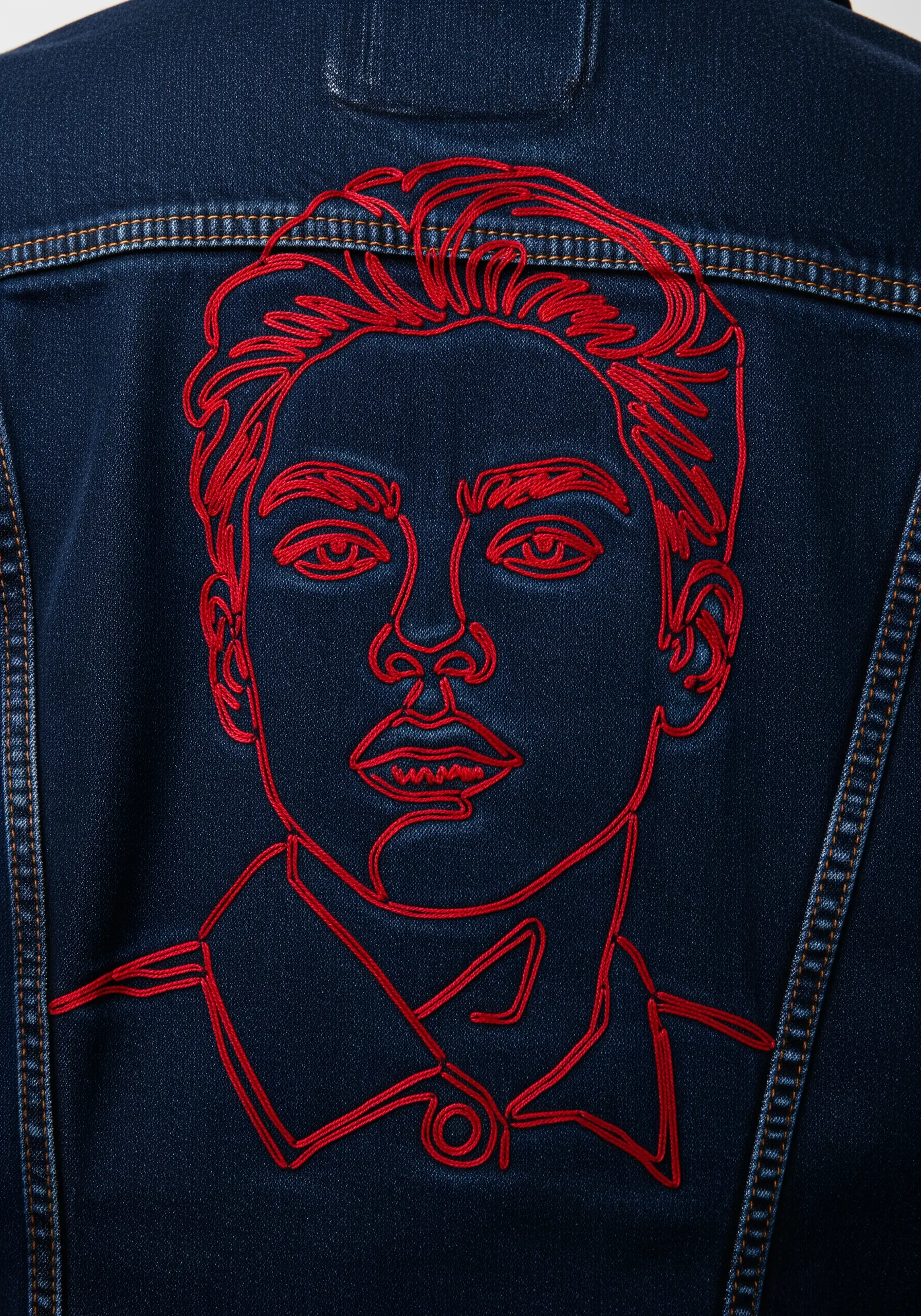 A bold, red line-art portrait of a man's face embroidered on a dark blue denim jacket.