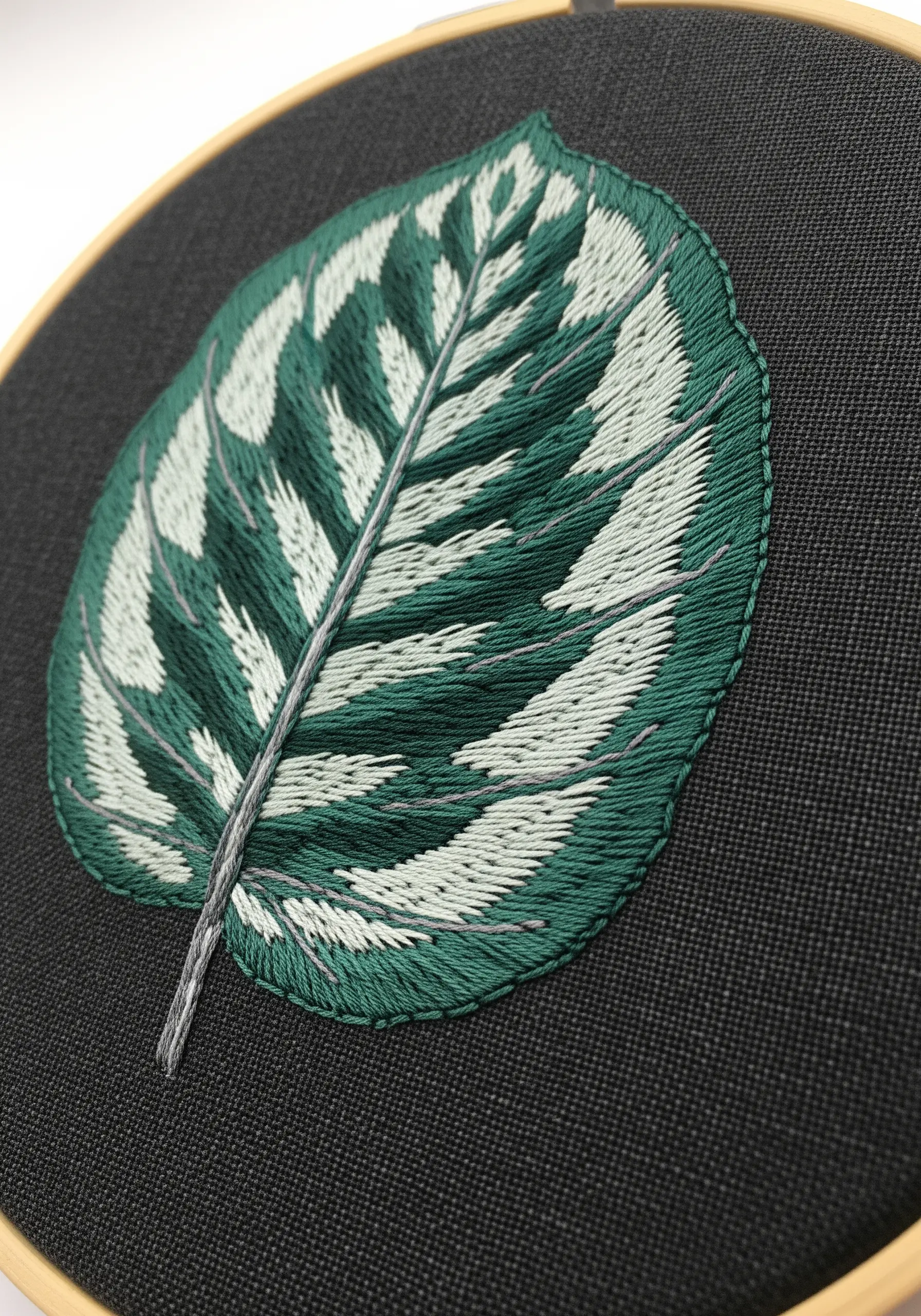 Embroidered Calathea leaf with bold green and white patterns on black fabric.