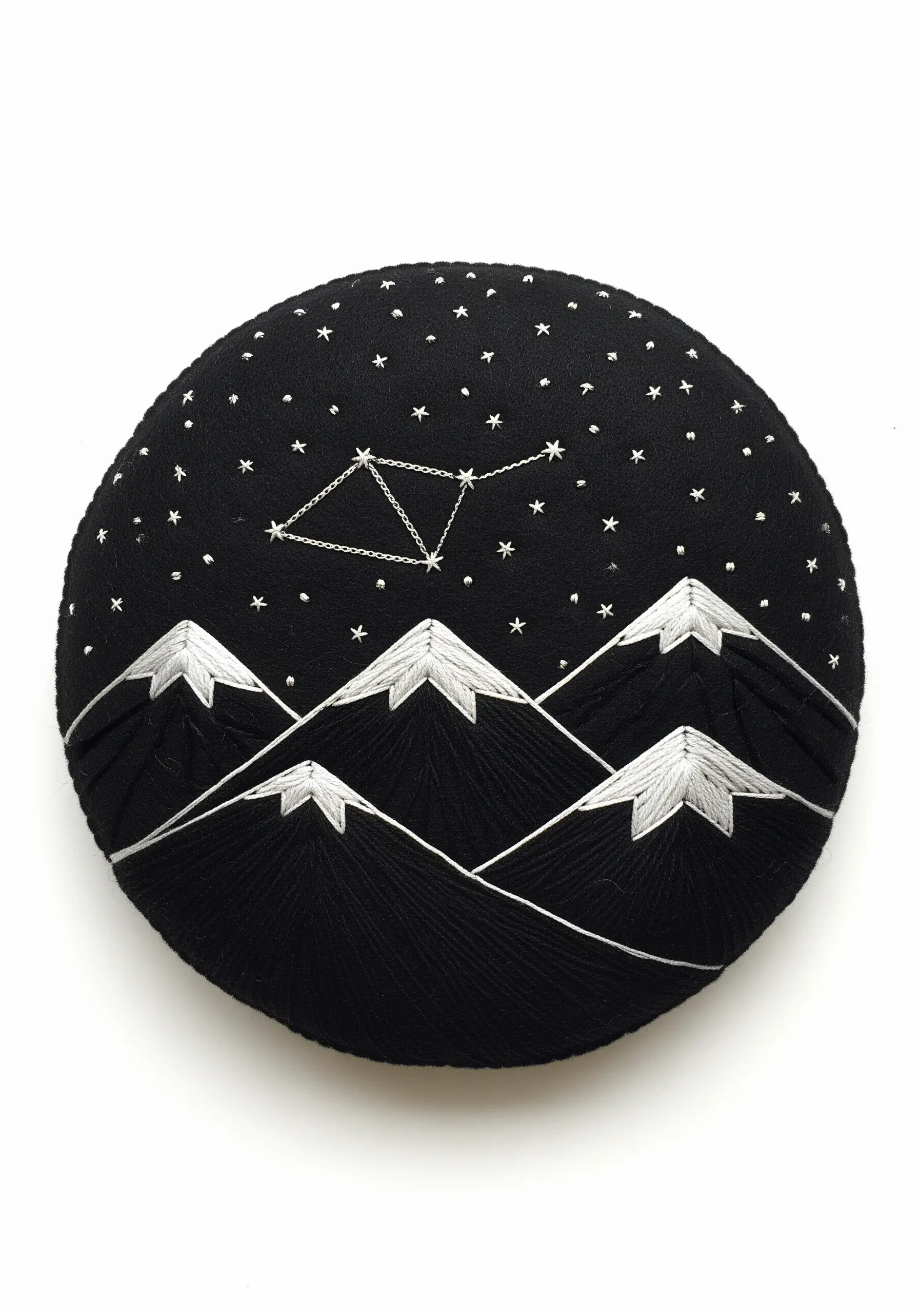 Minimalist embroidery of mountains and a constellation on a round black pillow.