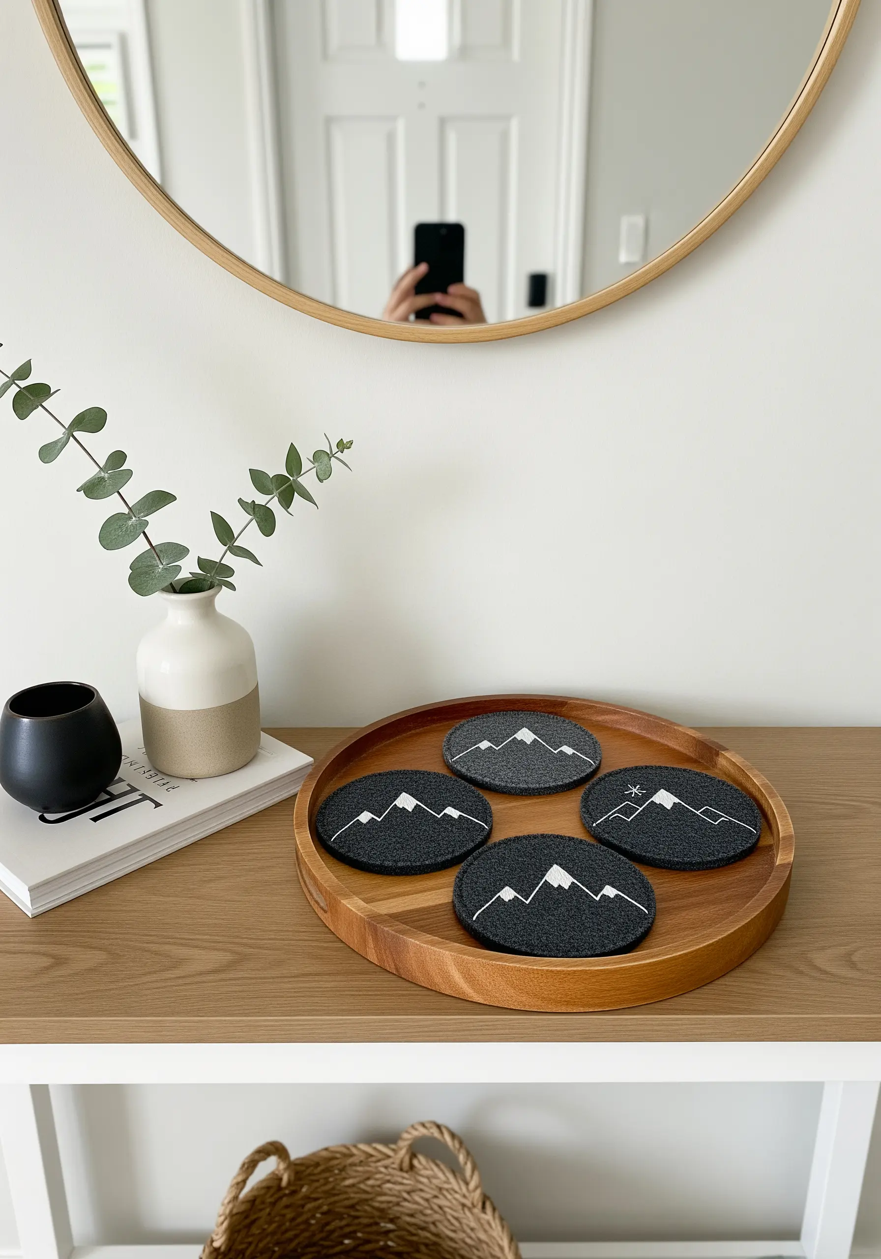 White line art embroidery of mountains on dark gray felt coasters.