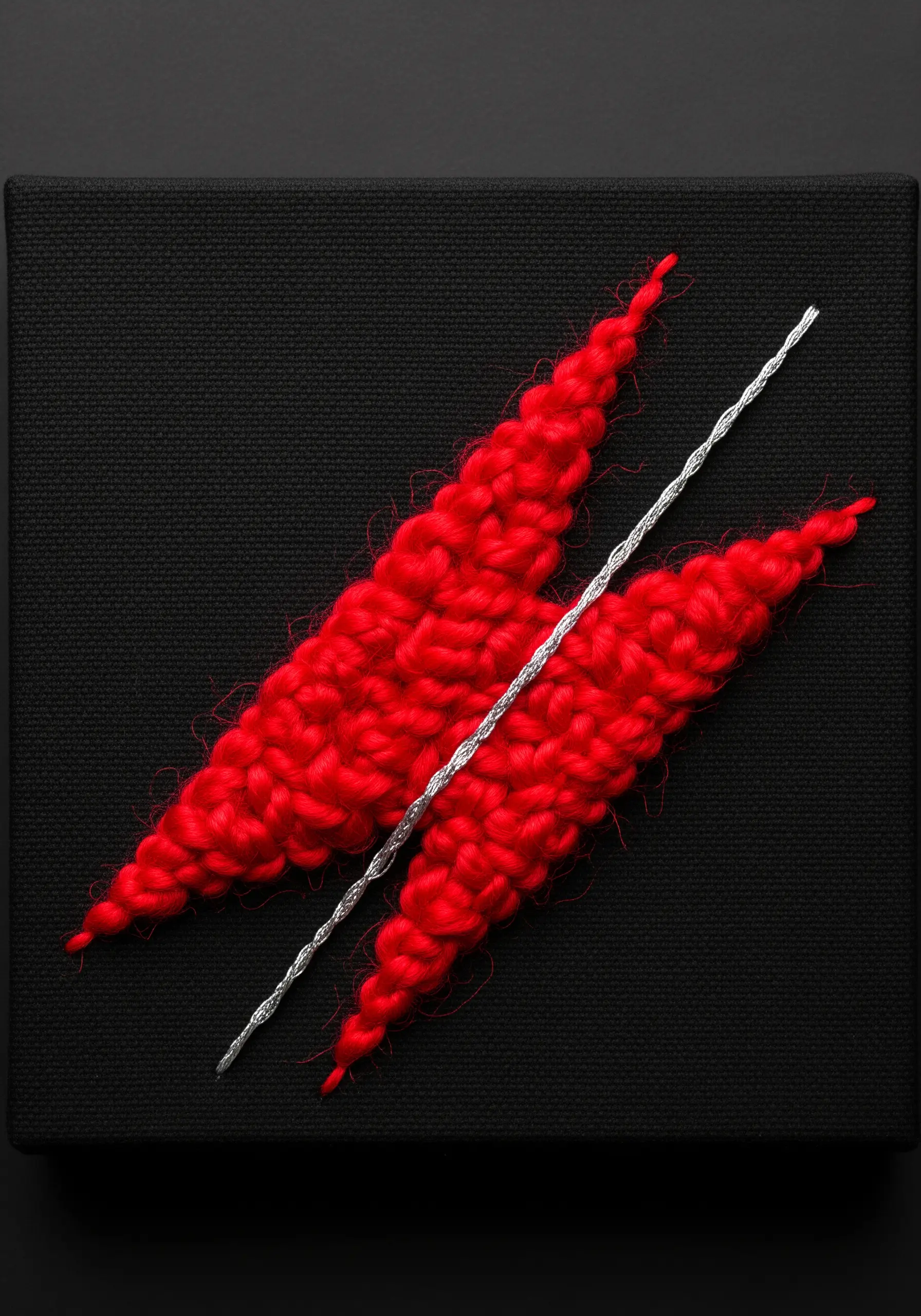 Abstract red chunky yarn embroidery contrasted with a thin silver cord on black canvas.