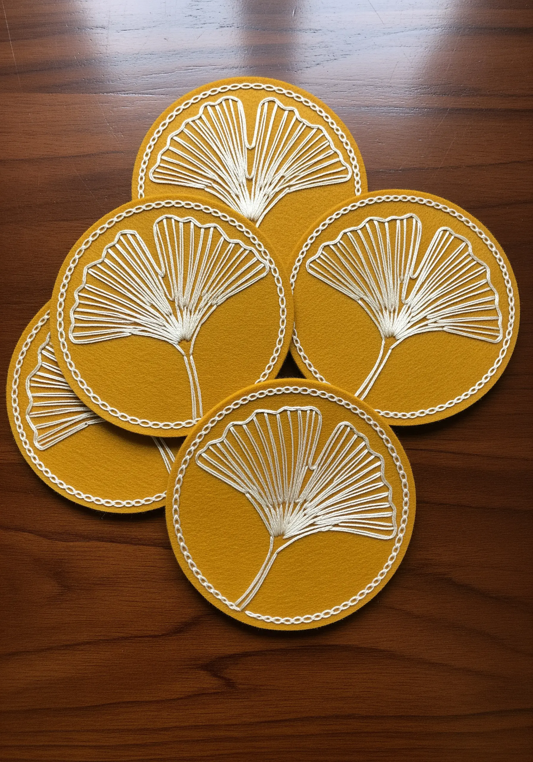 White line art ginkgo leaves embroidered onto mustard yellow felt coasters.