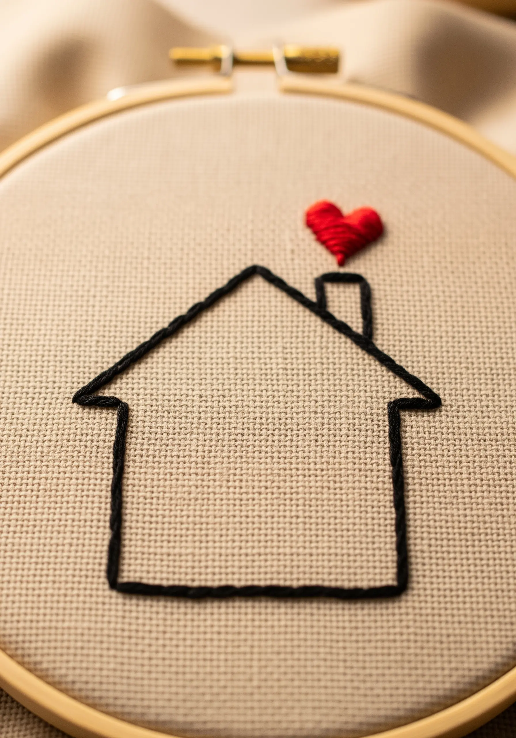 A simple backstitch outline of a house with a small, red padded satin stitch heart.