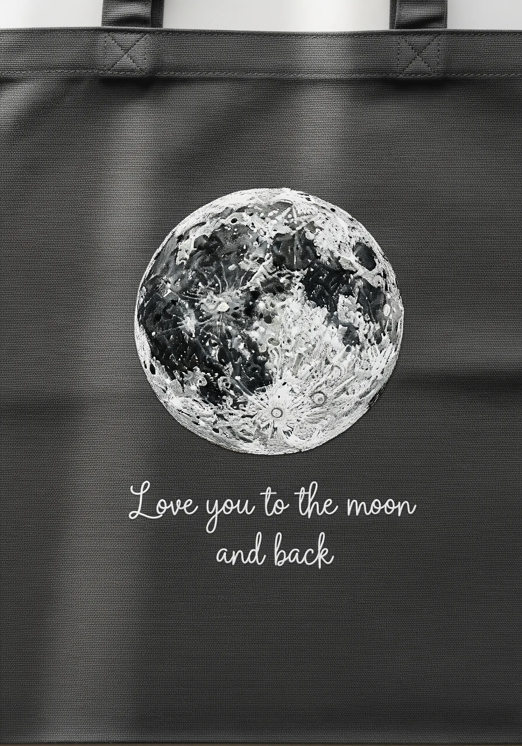 A highly detailed, textured embroidery of the full moon on a black tote with a romantic quote.