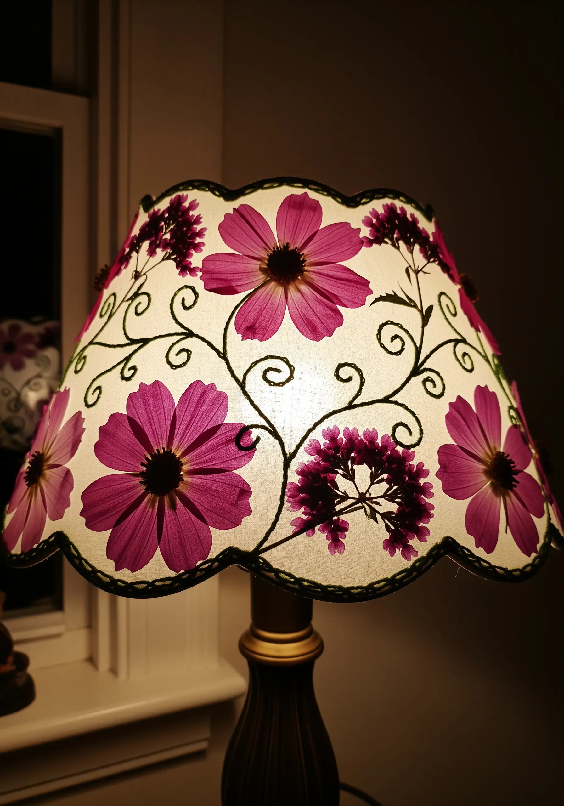 A lampshade decorated with glowing pink pressed cosmos flowers and embroidered vines.