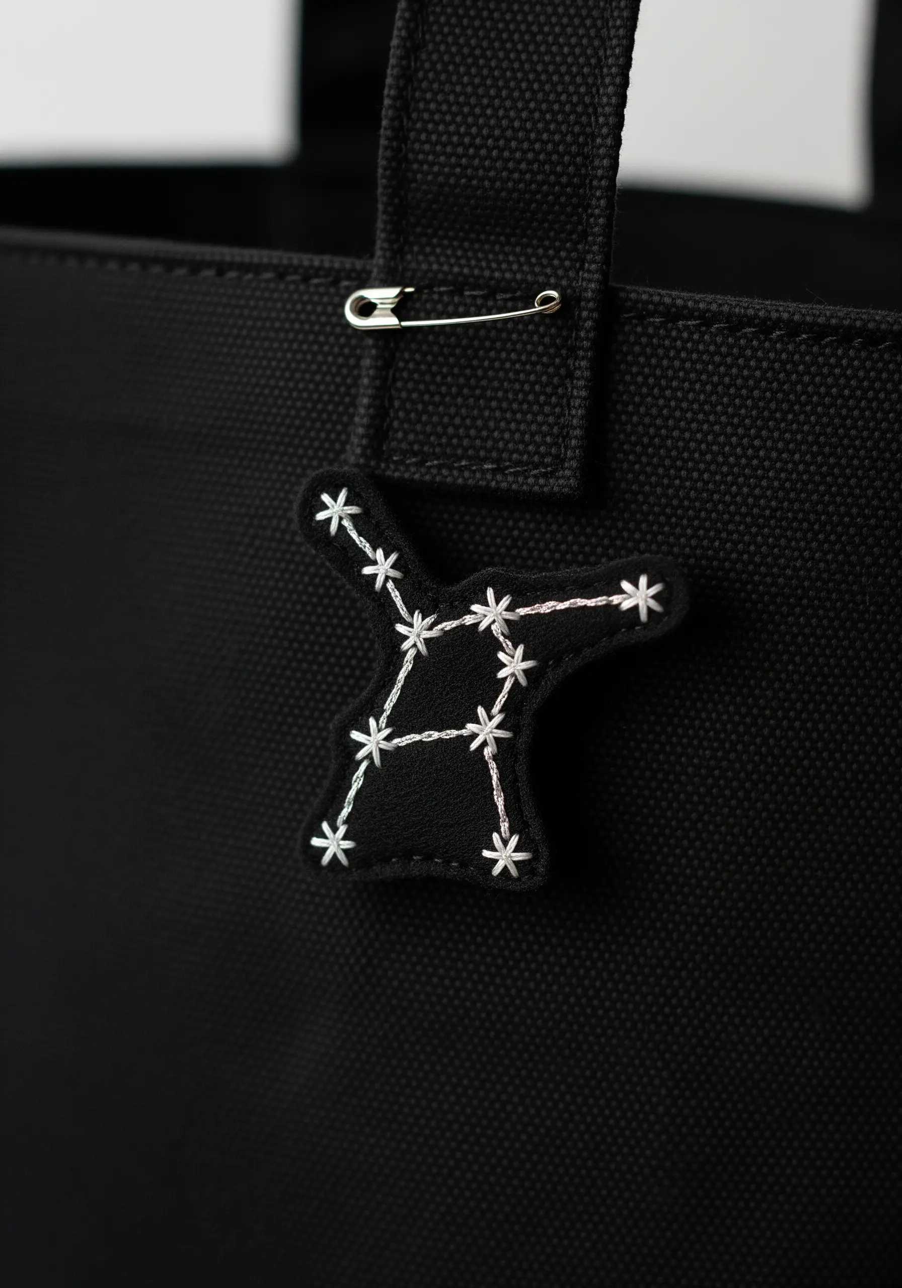 An embroidered constellation patch with star stitches pinned to a black tote bag.