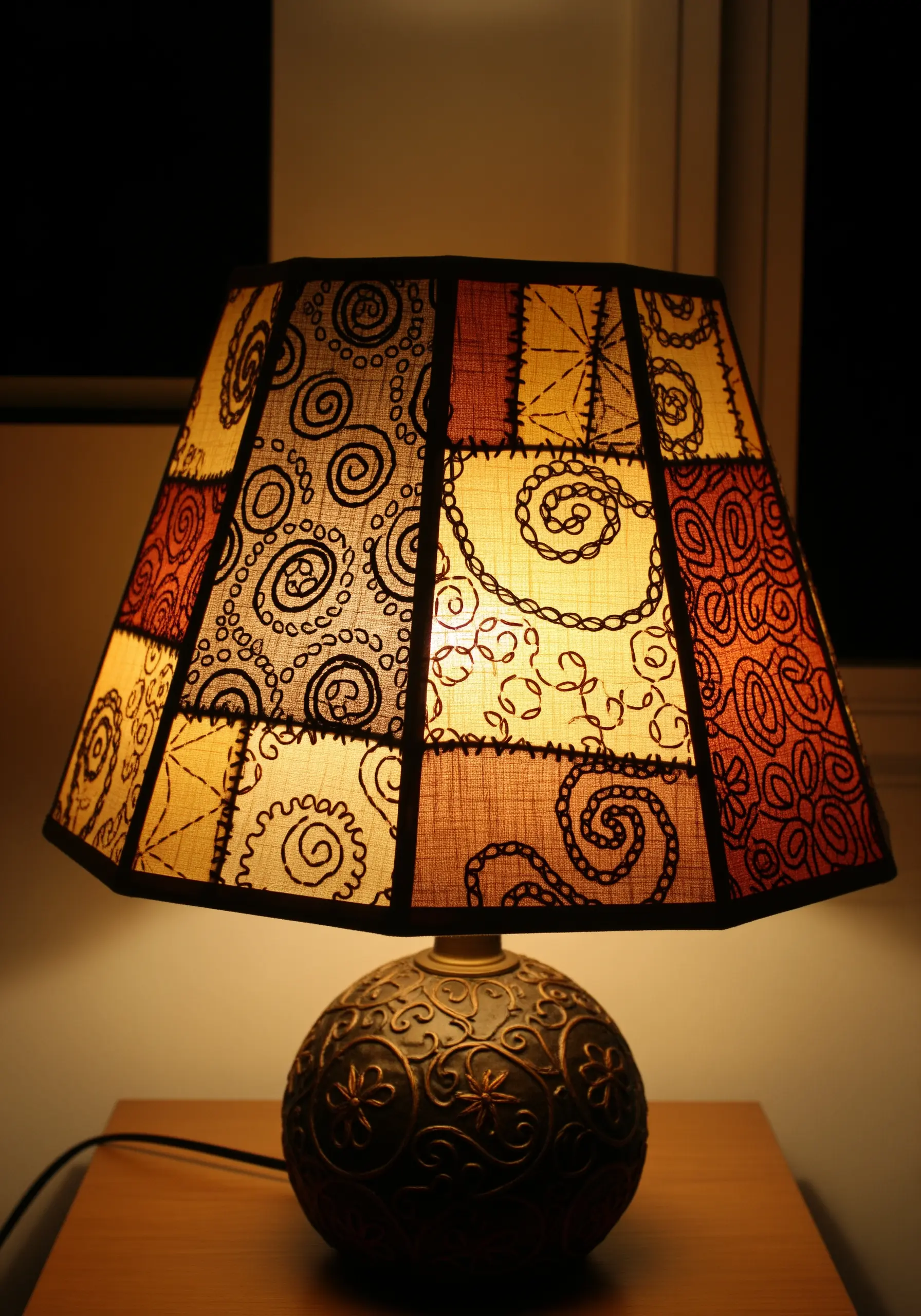 Patchwork lampshade with intricate blackwork embroidery patterns that are illuminated from within.